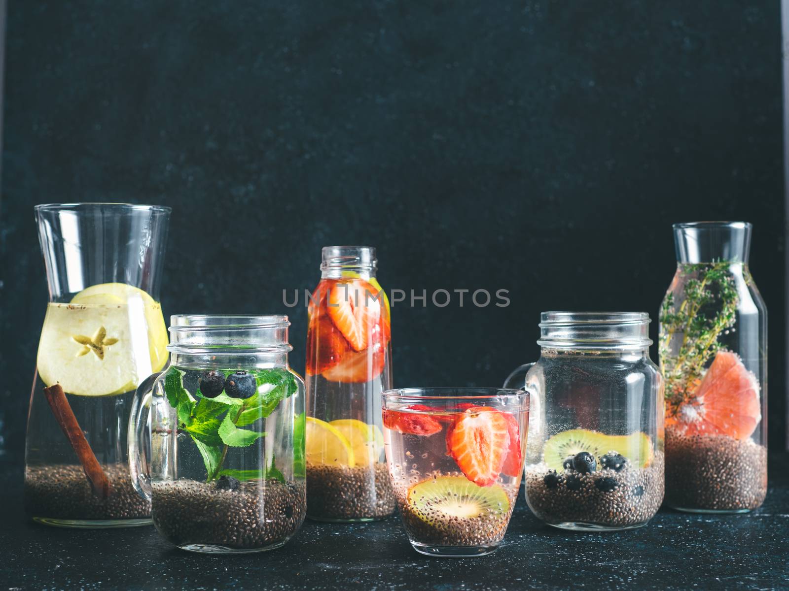 Different chia water in glass on dark background. Chia infused detox water with berries, fruits and herbs. Healthy eating, drinks, diet, detox concept. Copy space for text