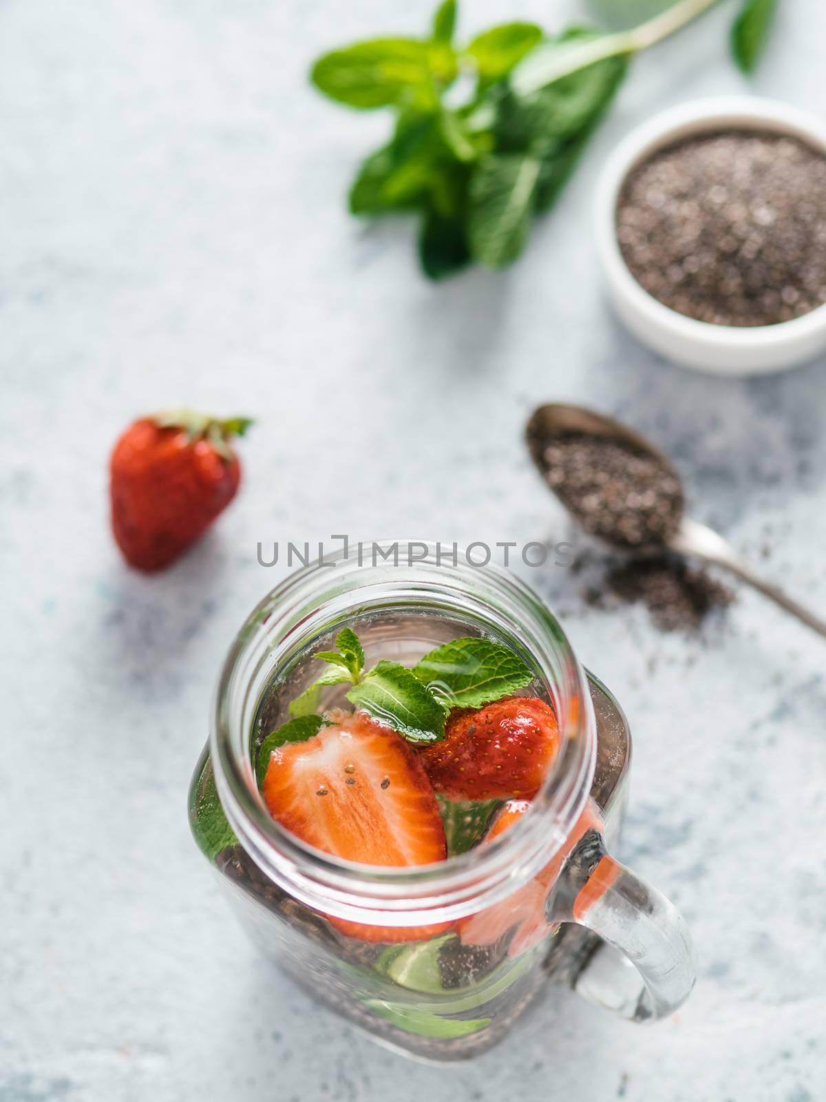 View from above chia water in mason jar with strawberry and mint on gray cement background. Chia infused detox water with berries. Healthy eating, drinks, diet, detox concept. Vertical