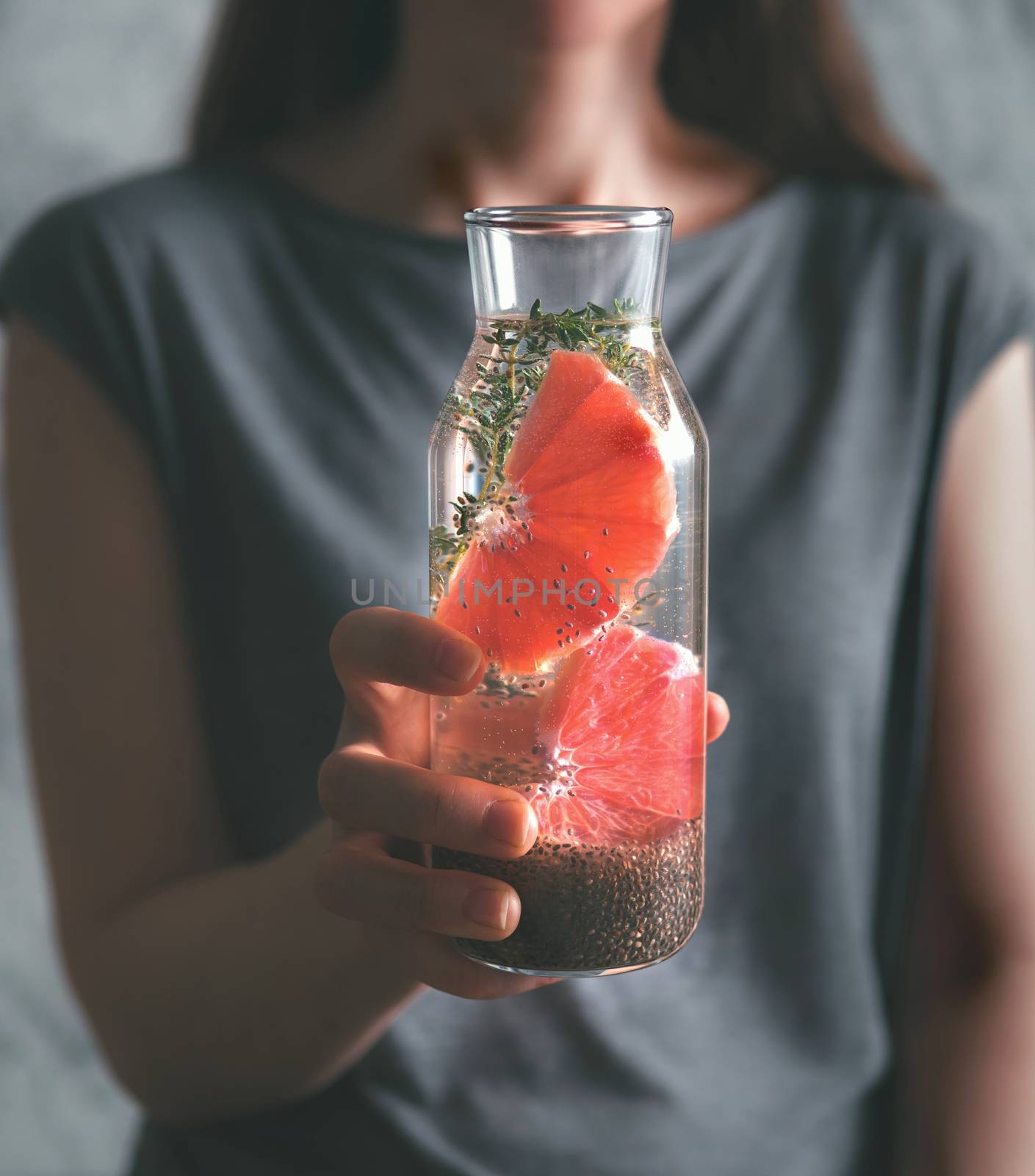 Woman hand with chia water. Glass bottle with chia detox water with grapefruit and thyme. Toned image. Dark or low key. Selective focus. Healthy eating, drinks, diet, detox and people concept