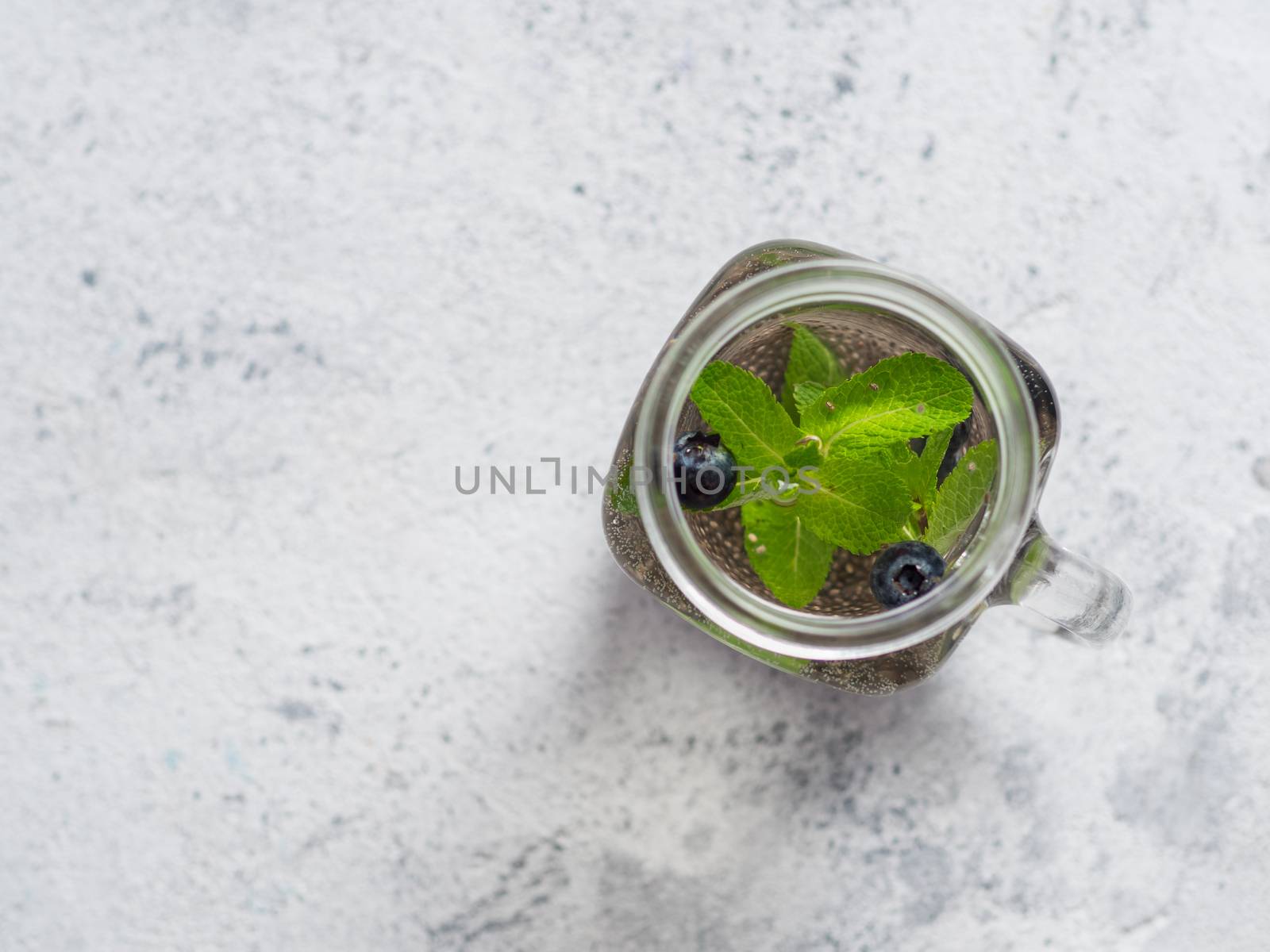 View from above chia water in mason jar with mint and blueberry on gray cement background.Chia infused detox water with berries.Copy space for text.Top view. Healthy eating, drinks, diet,detox concept