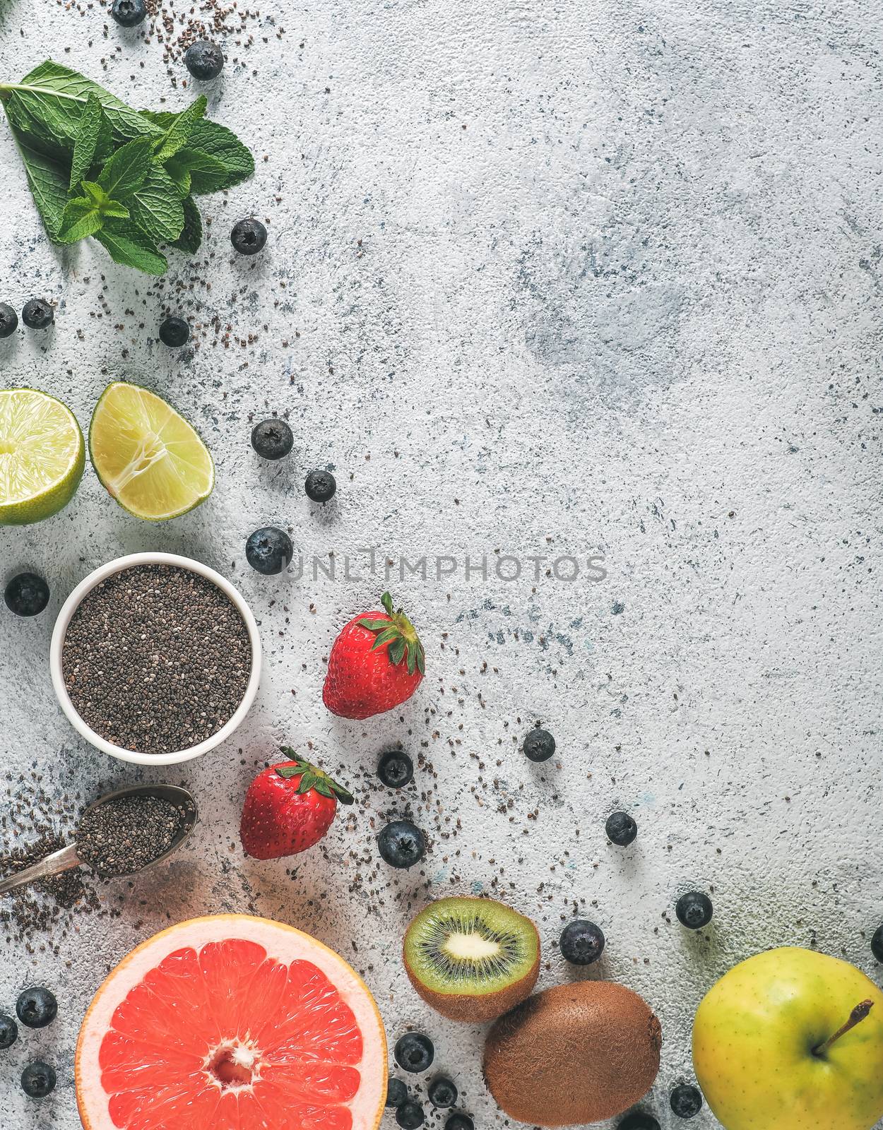 Ingredients for chia water and infused detox drink on gray background. Copy space. Above view,copy space. Fresh fruits, berries, chia seeds and mint. Healthy food, detox, diet, vegan concept. Vertical
