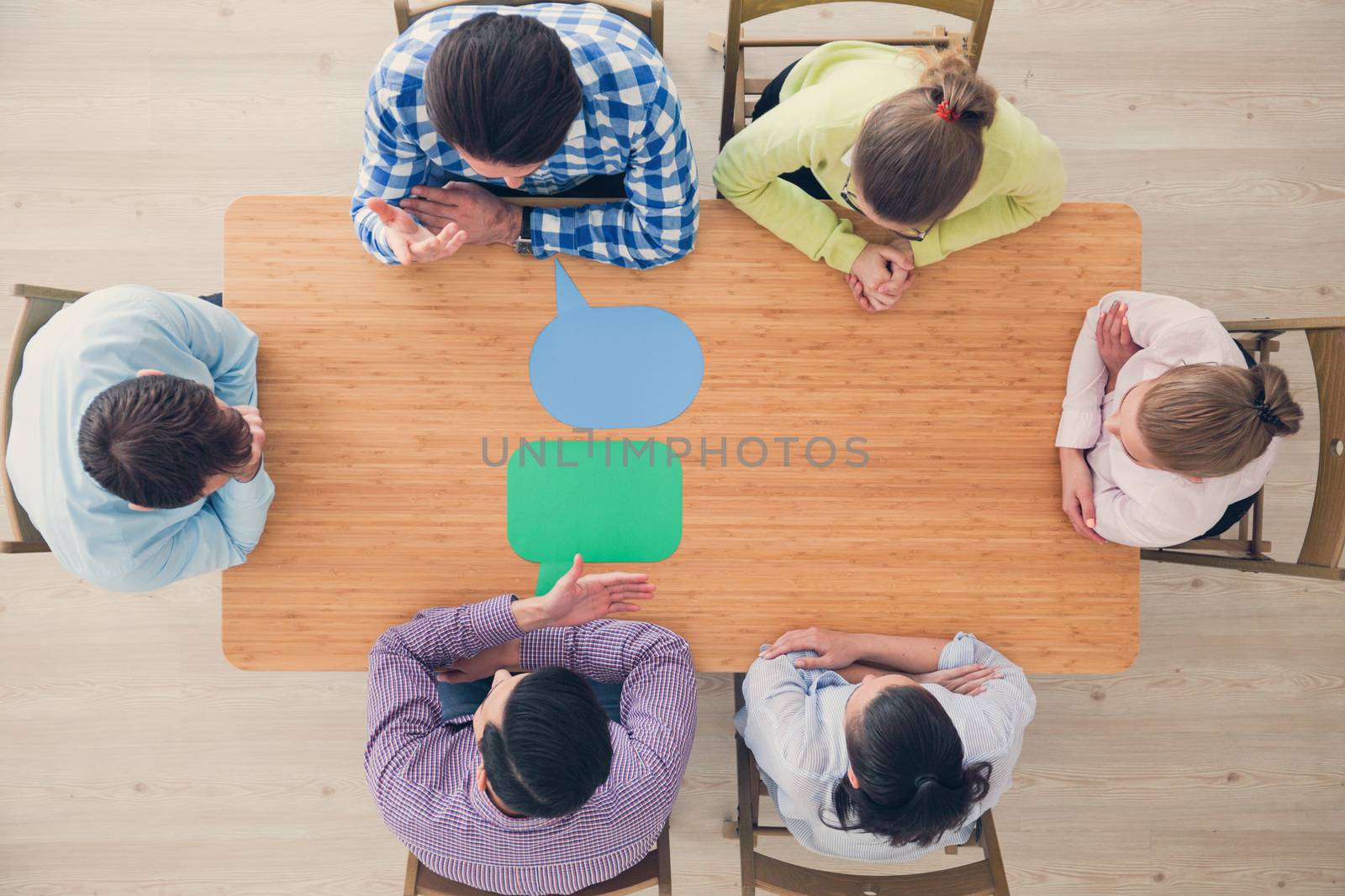 Team of business people in casual clothes sitting around the table with paper dialog boxes, discussing opinion concept