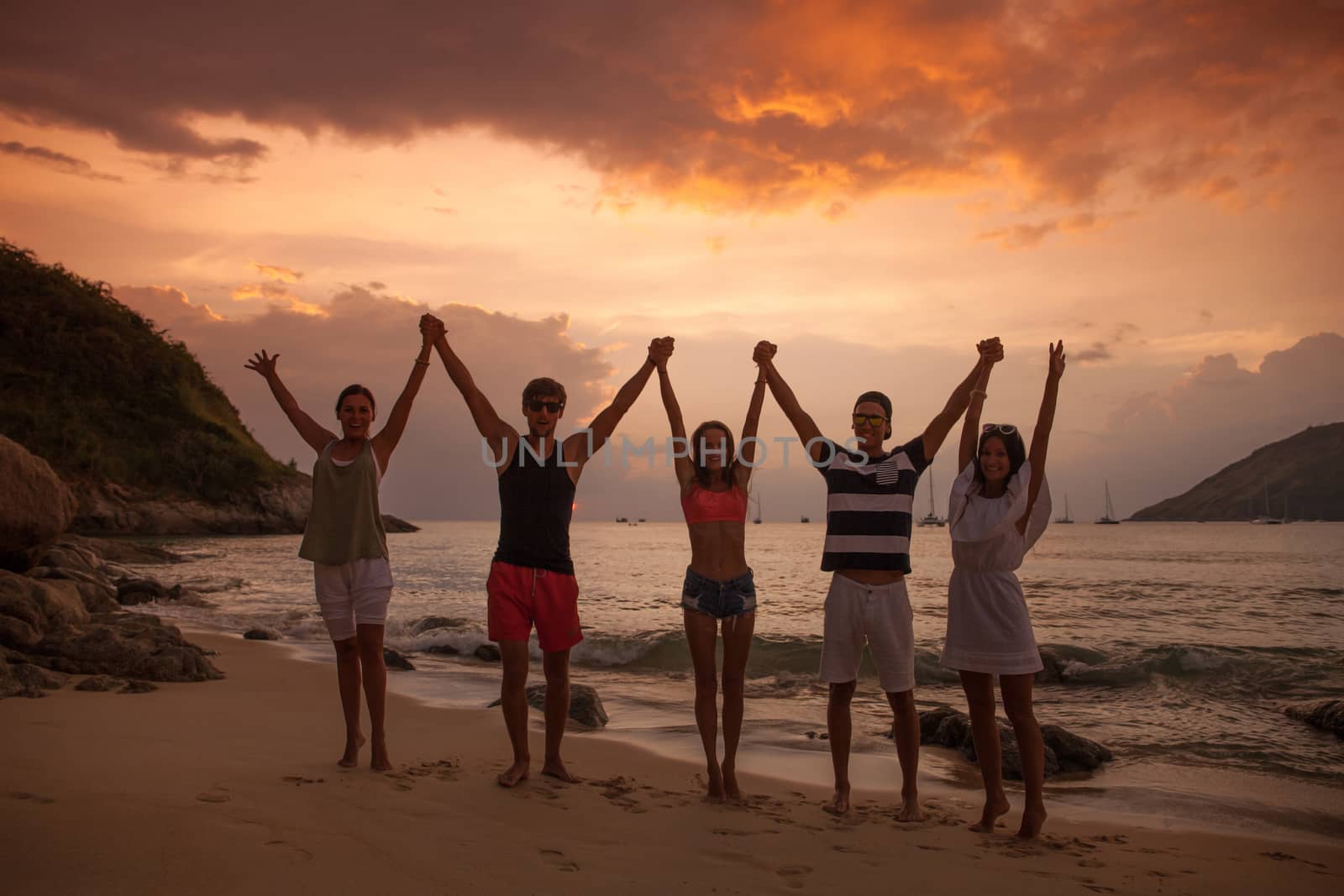 Group of happy people with raised hands at sea beach at sunset