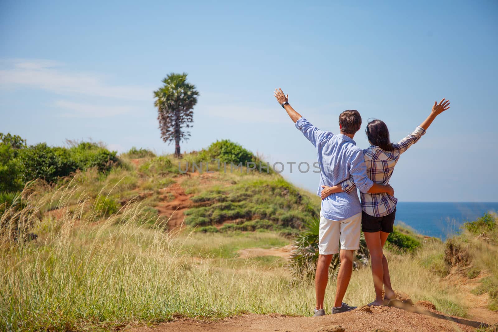 Young couple with raised hands hiking on hills near sea