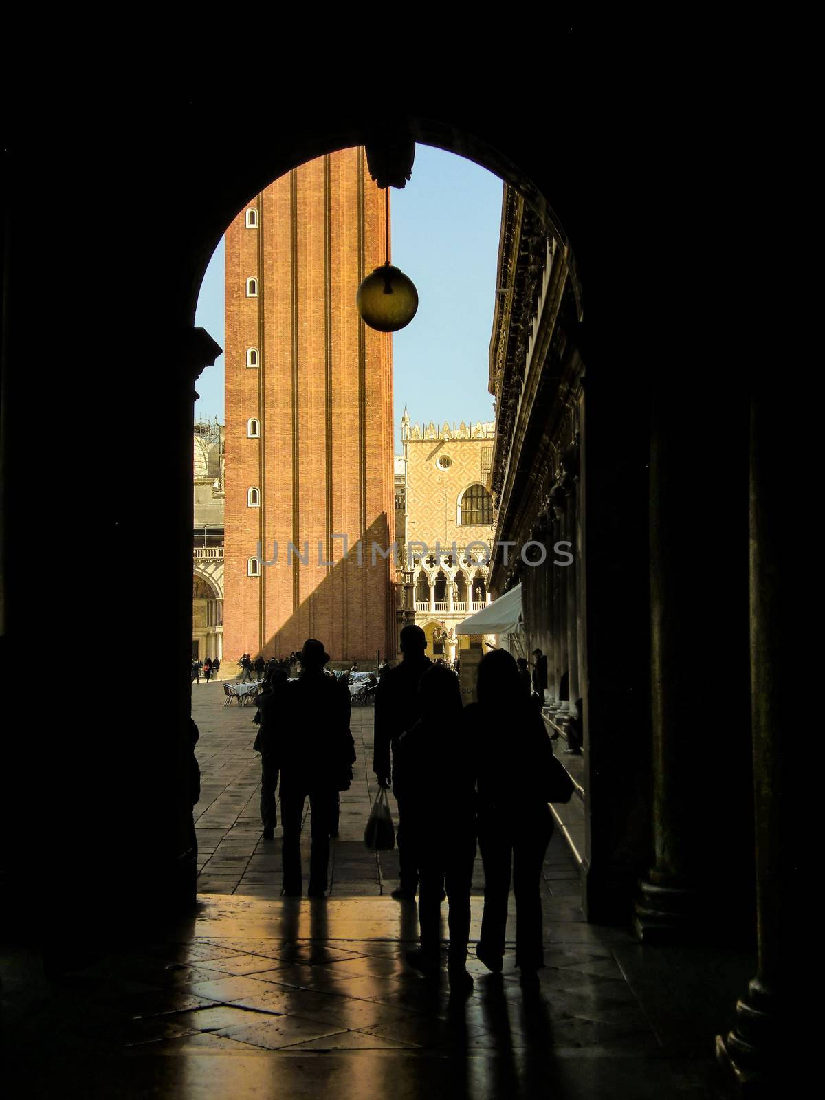 Arch or door in deep shadow behind Saint Mark square in Venice with tourists in shadow and shadow passing through.