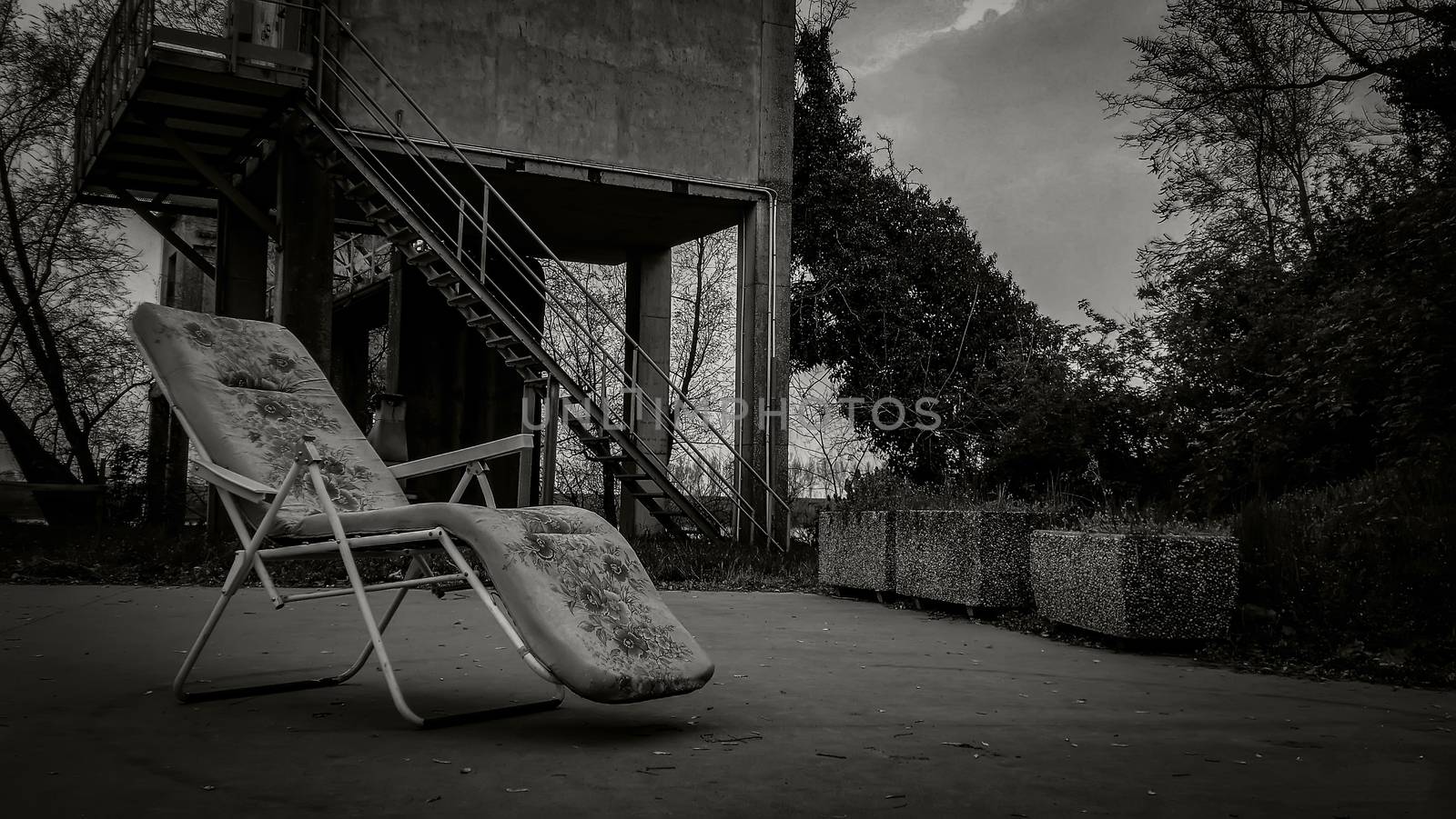 Composition with an old deck chair in an abandoned place with a very dull and gloomy appearance: a horror movie scenario.