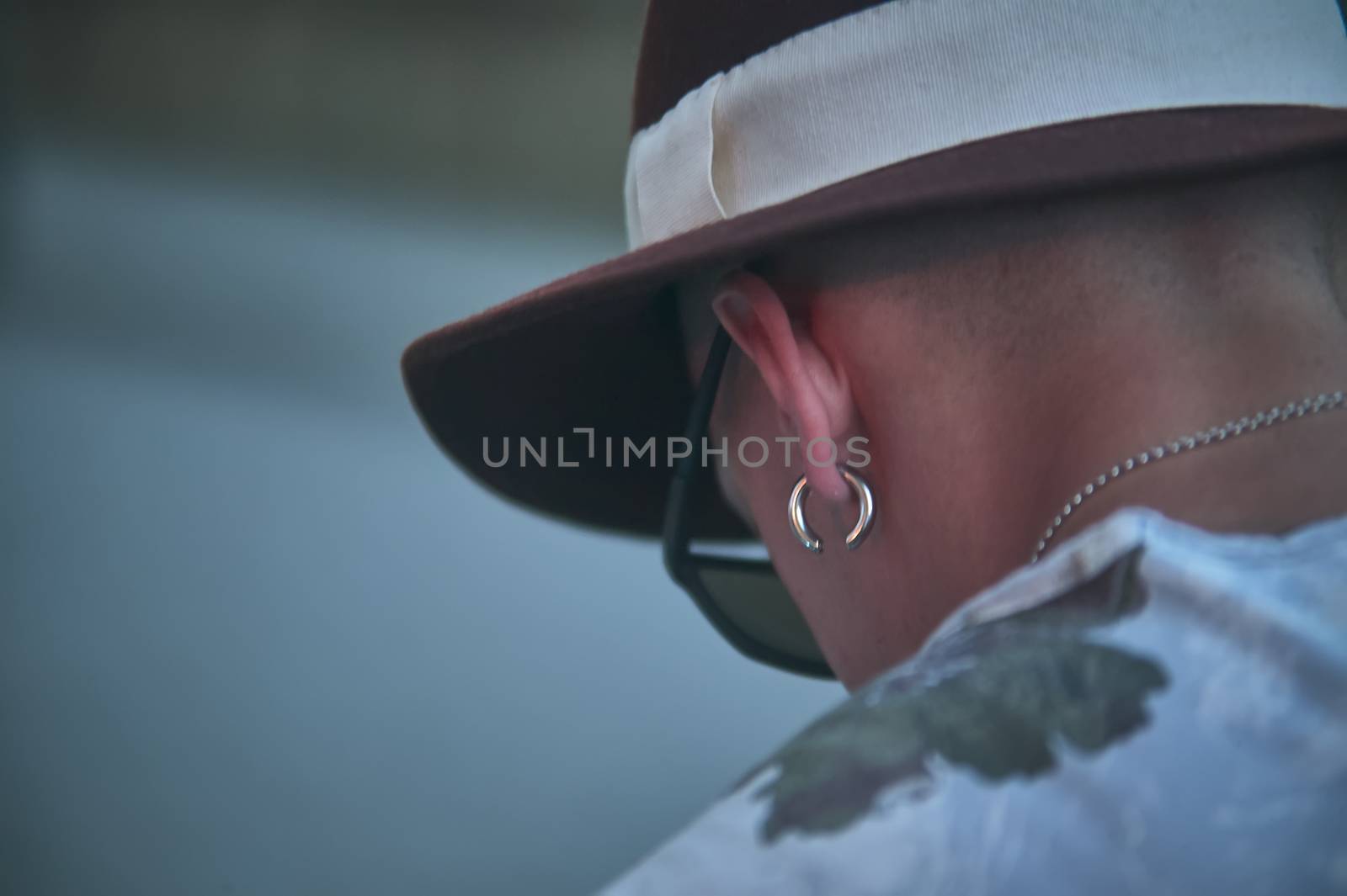 View of the neck and head of a boy with earrings and hat looking down. Symbol of sadness, depression and social discomfort.