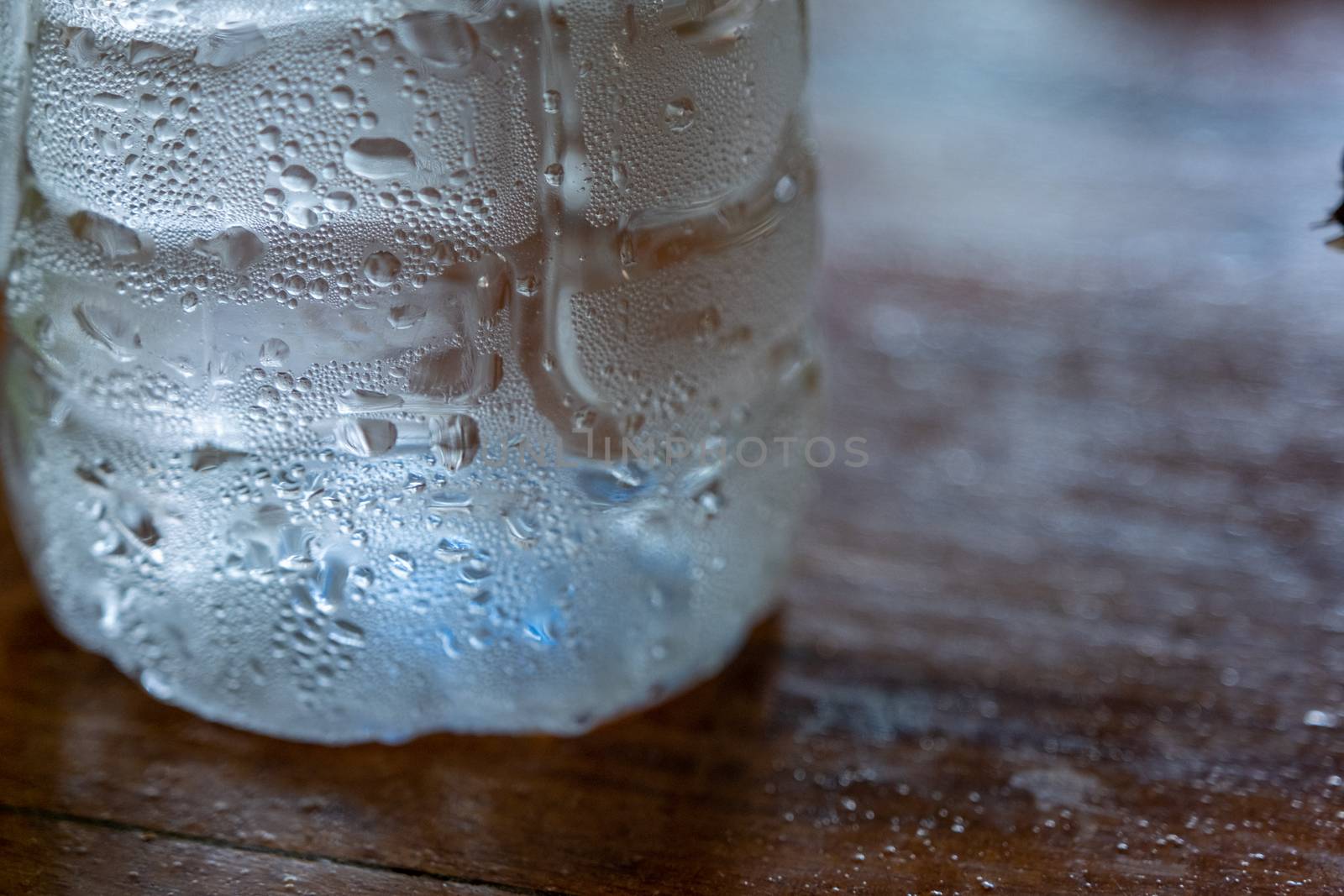 Clear water drop on cool water bottle on wooden table with blur background