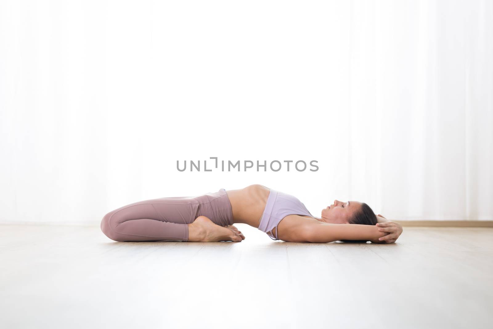Portrait of gorgeous active sporty young woman practicing yoga in studio. Beautiful girl practice Supta Vajrasana, fixed firm yoga pose. Healthy active lifestyle, working out indoors in gym.