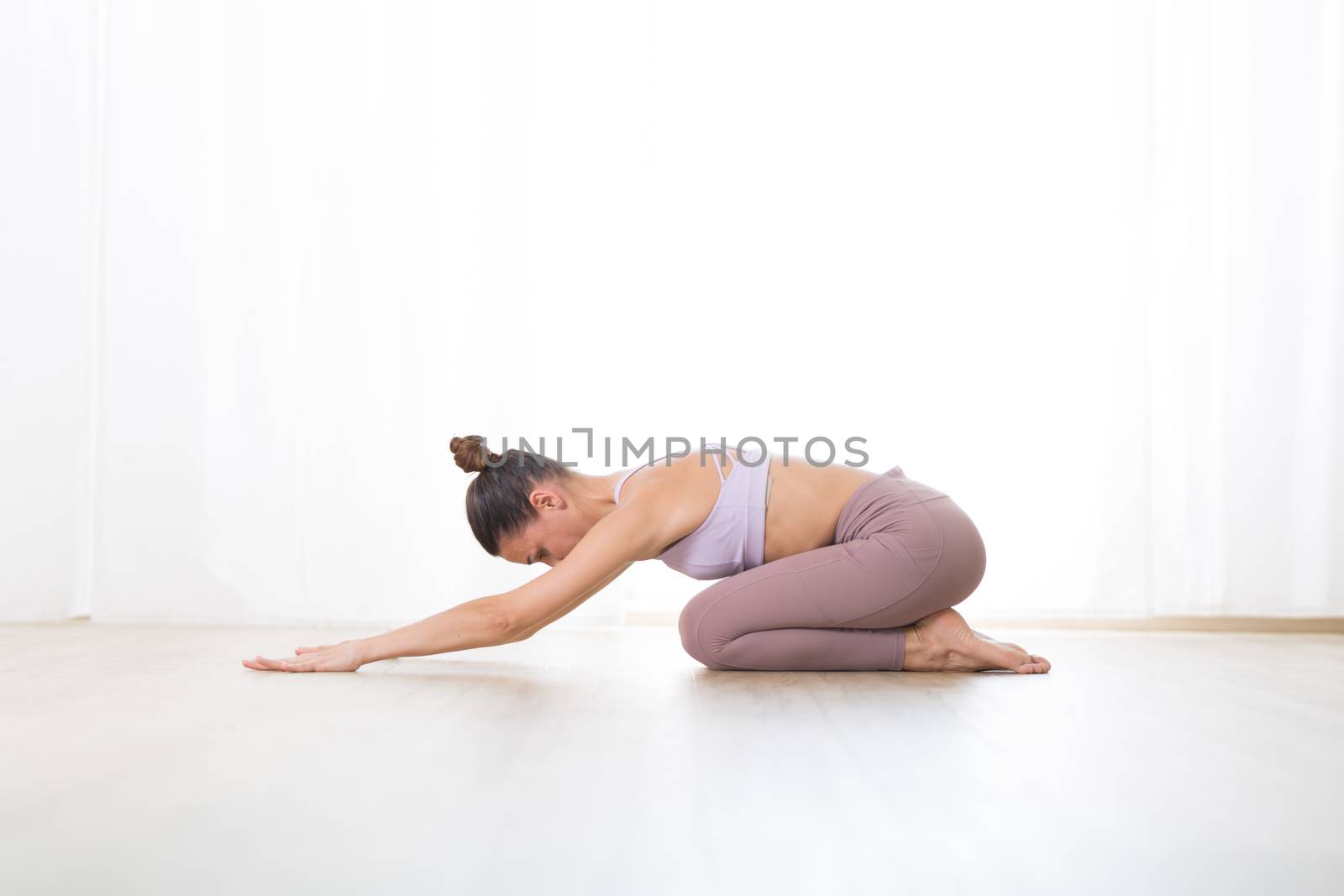 Portrait of gorgeous active sporty young woman practicing yoga in studio. Beautiful girl practice Ardha Kurmasana, half tortoise yoga pose. Healthy active lifestyle, working out indoors in gym.