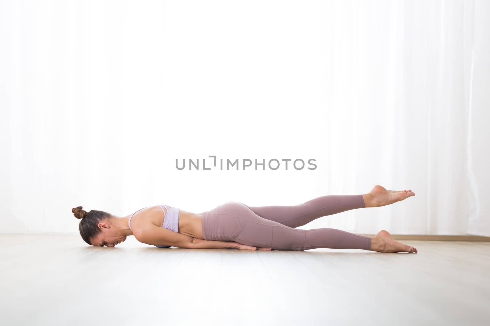 Portrait of gorgeous active sporty young woman practicing yoga in studio. Beautiful girl practice Salabhasana, locust yoga pose. Healthy active lifestyle, working out indoors in gym.