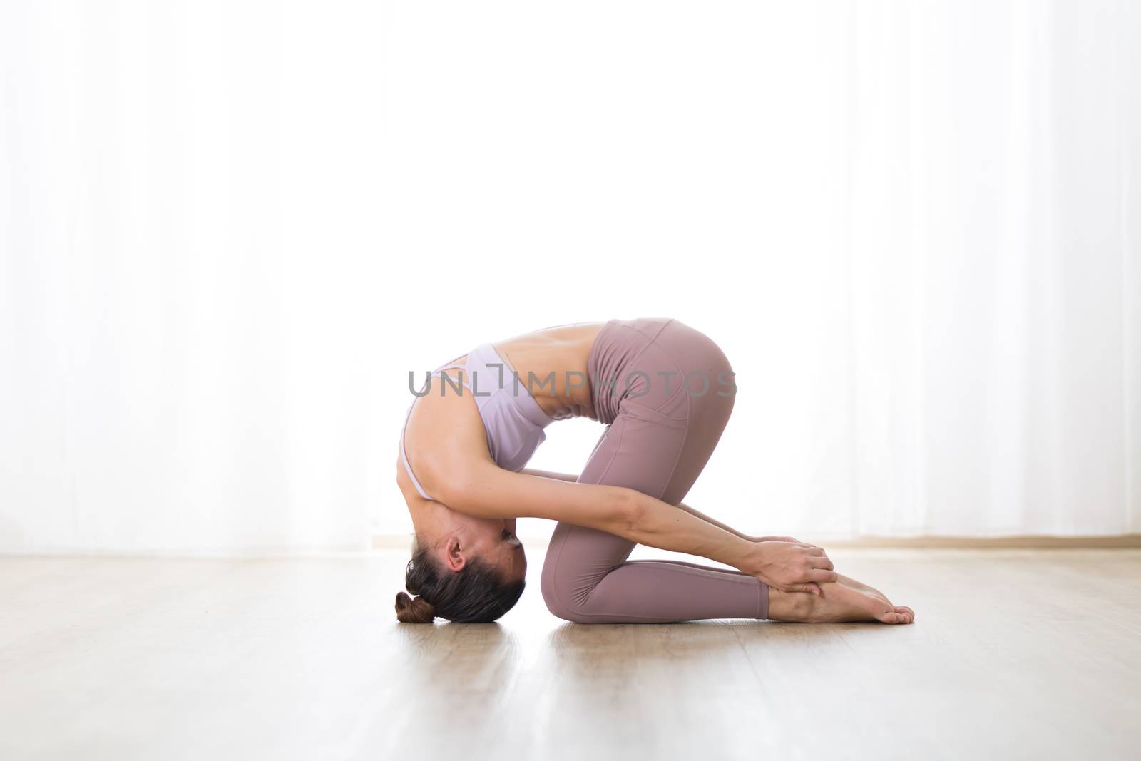 Portrait of gorgeous active sporty young woman practicing yoga in studio. Beautiful girl practice Sasangasana, rabbit yoga pose. Healthy active lifestyle, working out indoors in gym.