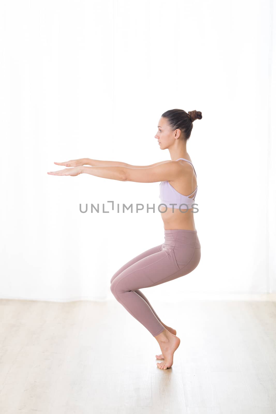 Portrait of gorgeous active sporty young woman practicing yoga in studio. Beautiful girl practice Utkatasana, awkward yoga pose. Healthy active lifestyle, working out in gym by kasto