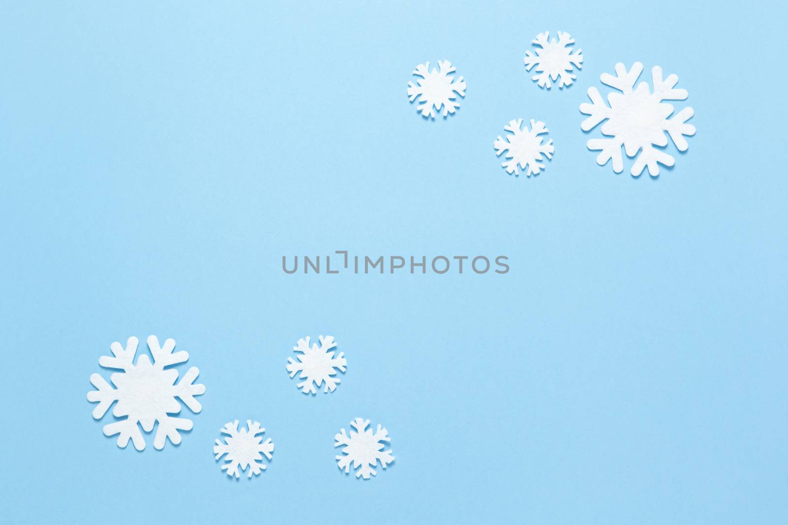 Christmas composition, group of little white felt snowflakes on pastel blue background, copy space. Festive, New Year concept. Horizontal, flat lay. Minimal style. Top view.