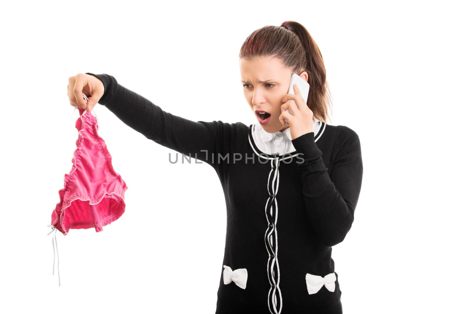 Cheating, adultery concept. Angry young woman holding someone else's panties while talking on the phone, looking disgusted, isolated on white background.