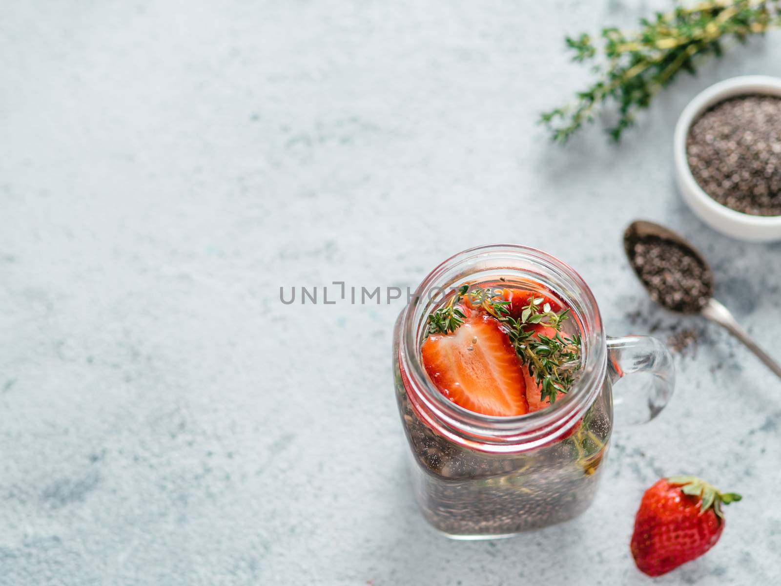 View from above chia water in mason jar with strawberry and thyme on gray cement background. Chia infused detox water with berries. Copy space for text. Healthy eating, drinks, diet, detox concept