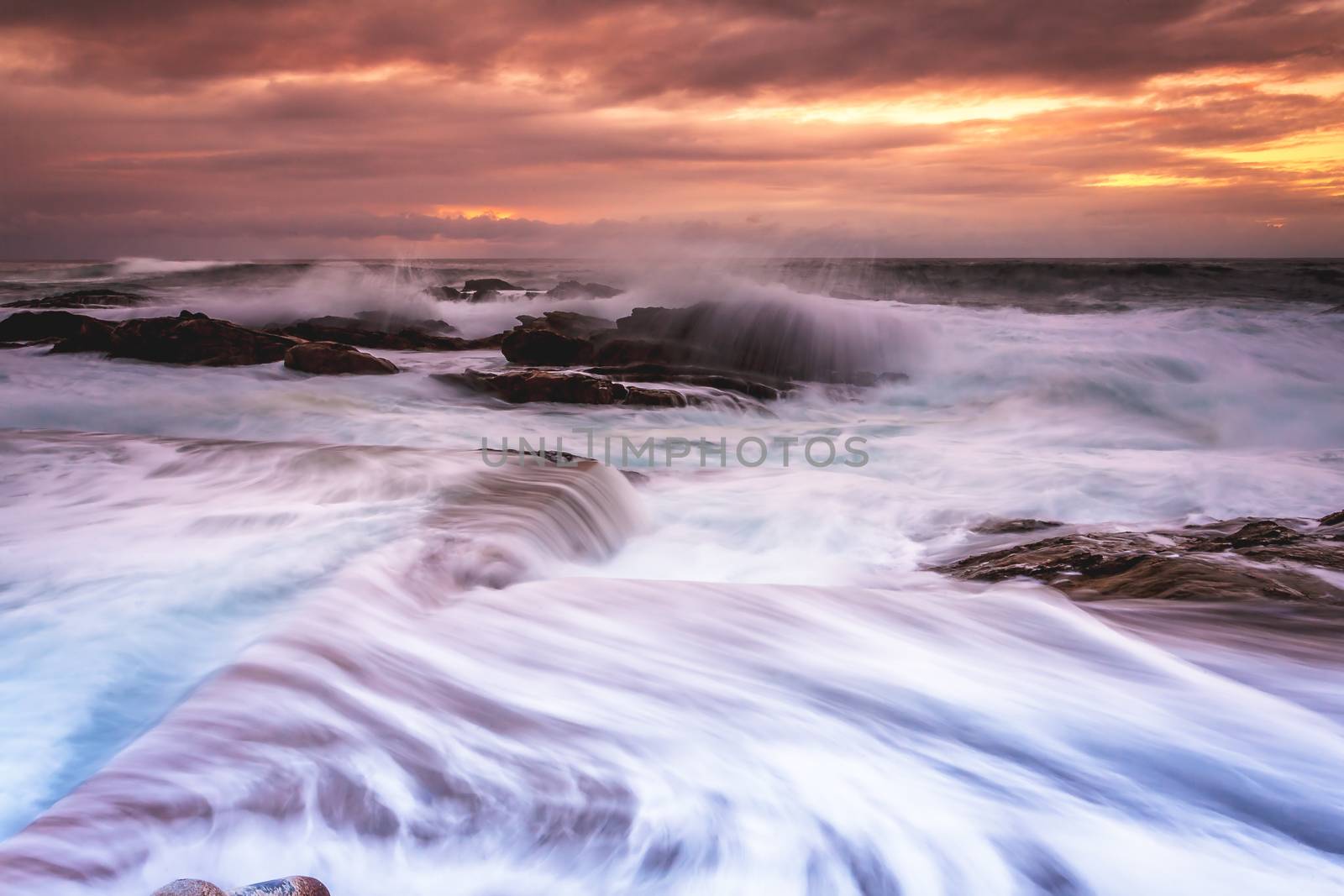 Big swell and large waves flow into the ocean tidal pools just after sunrise the motion of the flows creating interesting movement and texture.