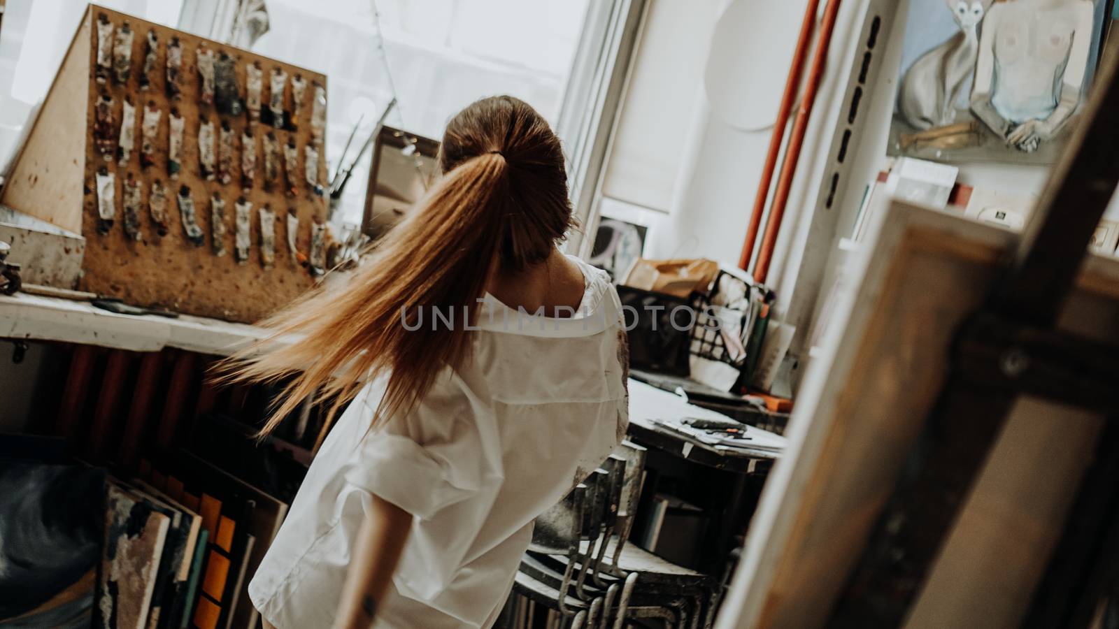 Beautiful female painter wearing white shirt dancing while painting in art workshop. Selective focus. Vintage style photo