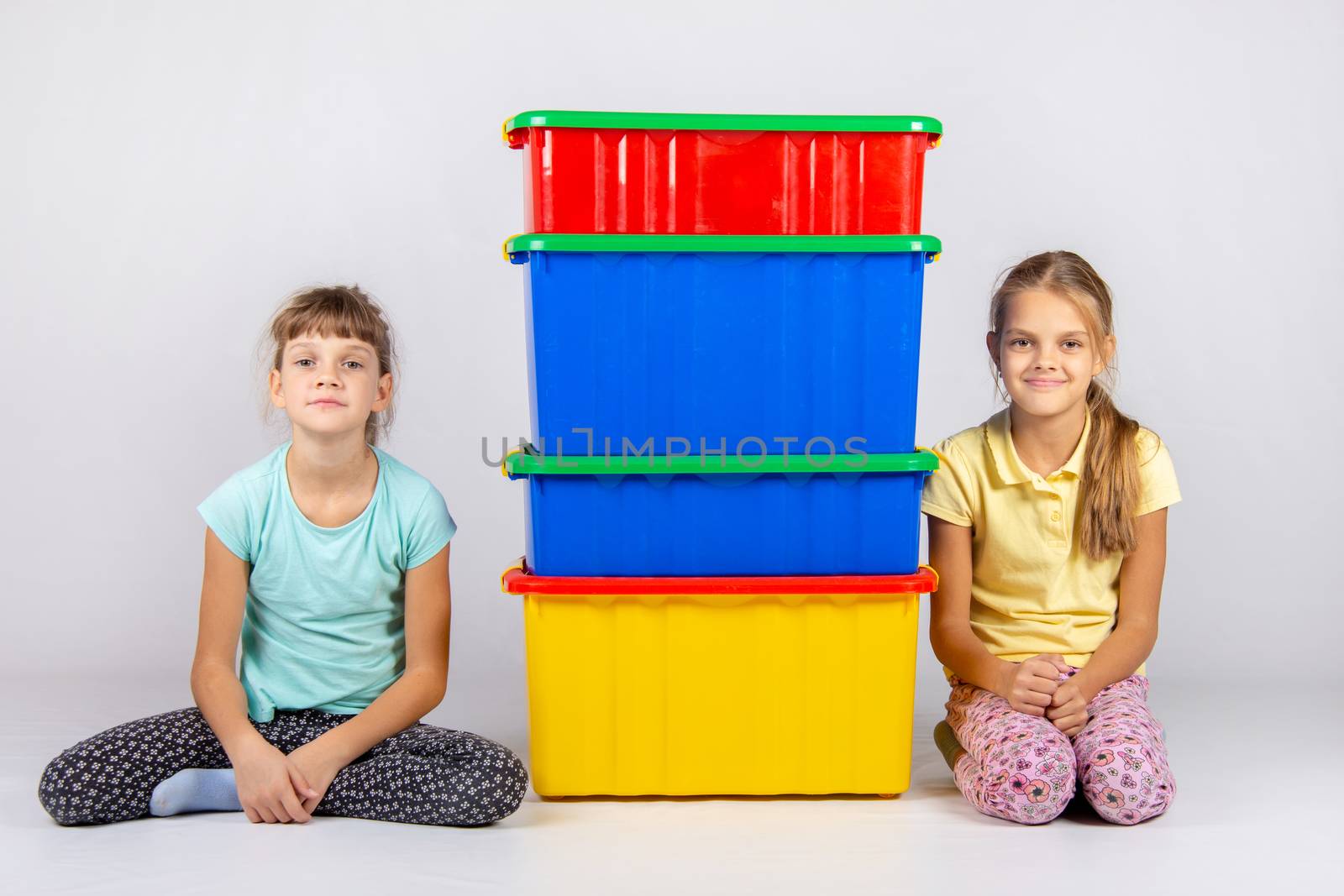 Two girls are sitting next to four large plastic boxes