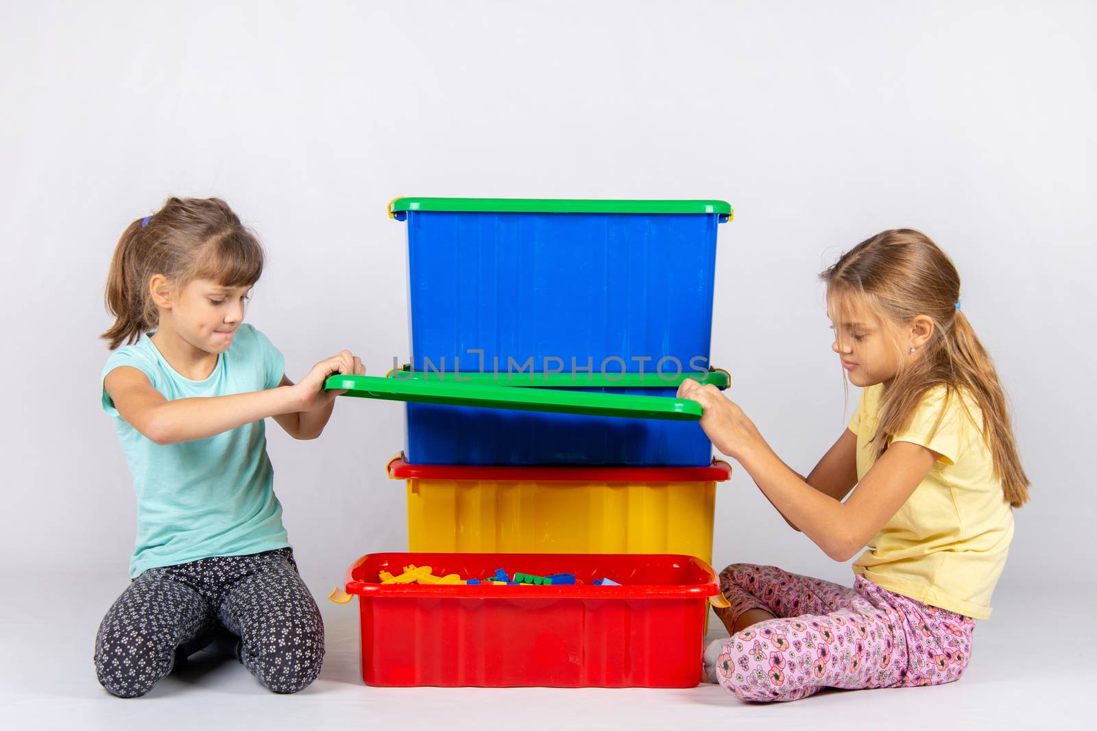 Two girls opened a large plastic box with toys