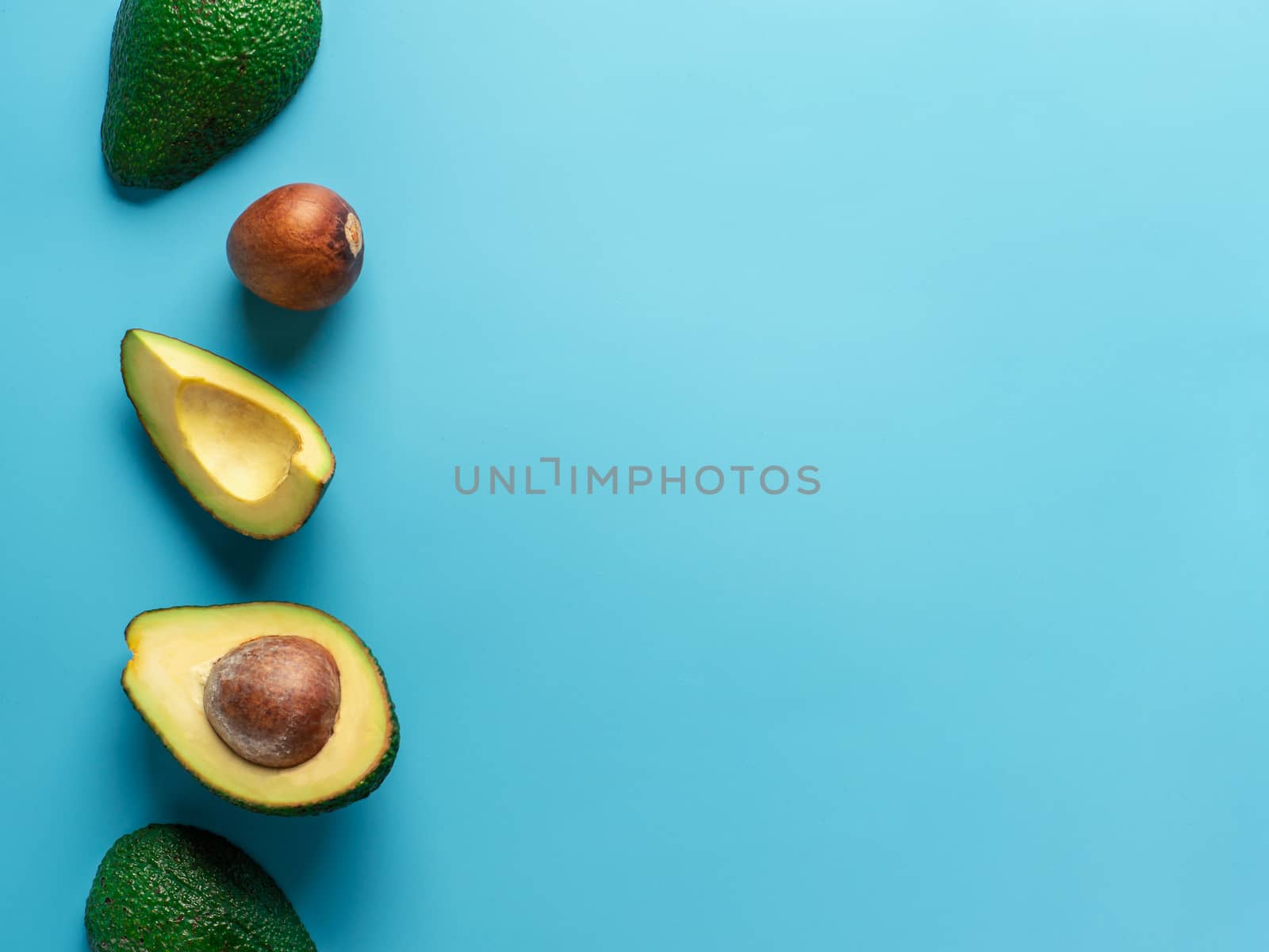 Avocado with copy space. Top view of avocado half, quarter and avocado pit on bright blue background. Food background