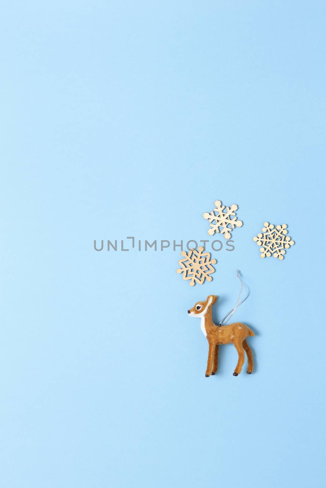 Christmas decoration, naturalistic toy roe deer and three little wooden snowflakes on pastel blue background, copy space. Festive, New Year concept. Vertical, flat lay. Minimal style. Top view.