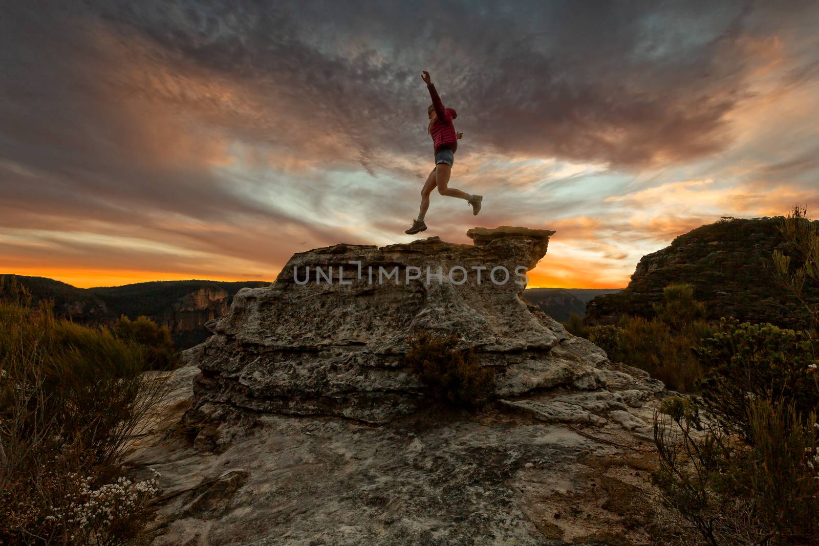 Active woman jumping on mountain cliffs at sunset by lovleah