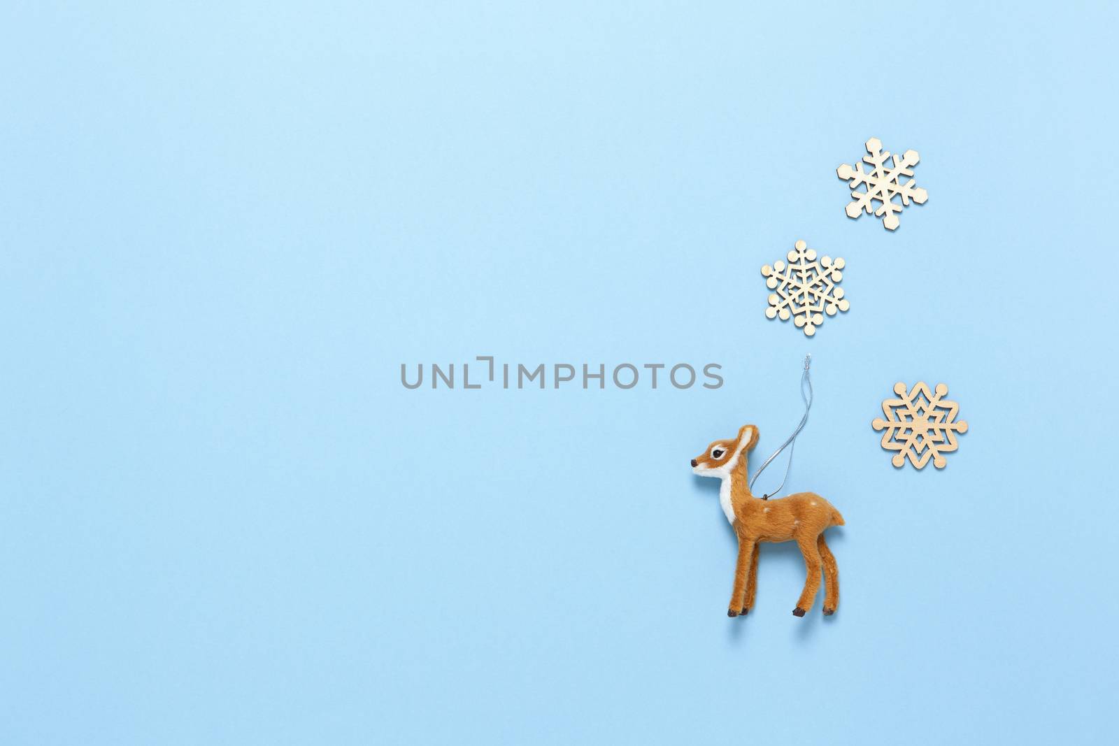 Christmas decoration, naturalistic toy roe deer and three little wooden snowflakes on pastel blue background, copy space. Festive, New Year concept. Horizontal, flat lay. Minimal style. Top view.