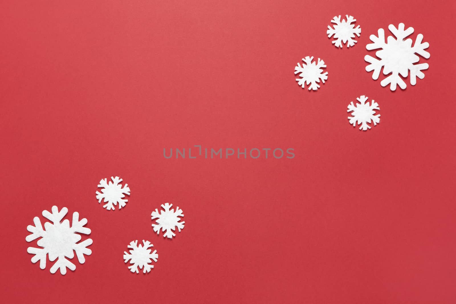 Christmas composition, group of little white felt snowflakes on burgundy red background, copy space. Festive, New Year concept. Horizontal, flat lay. Minimal style. Top view.
