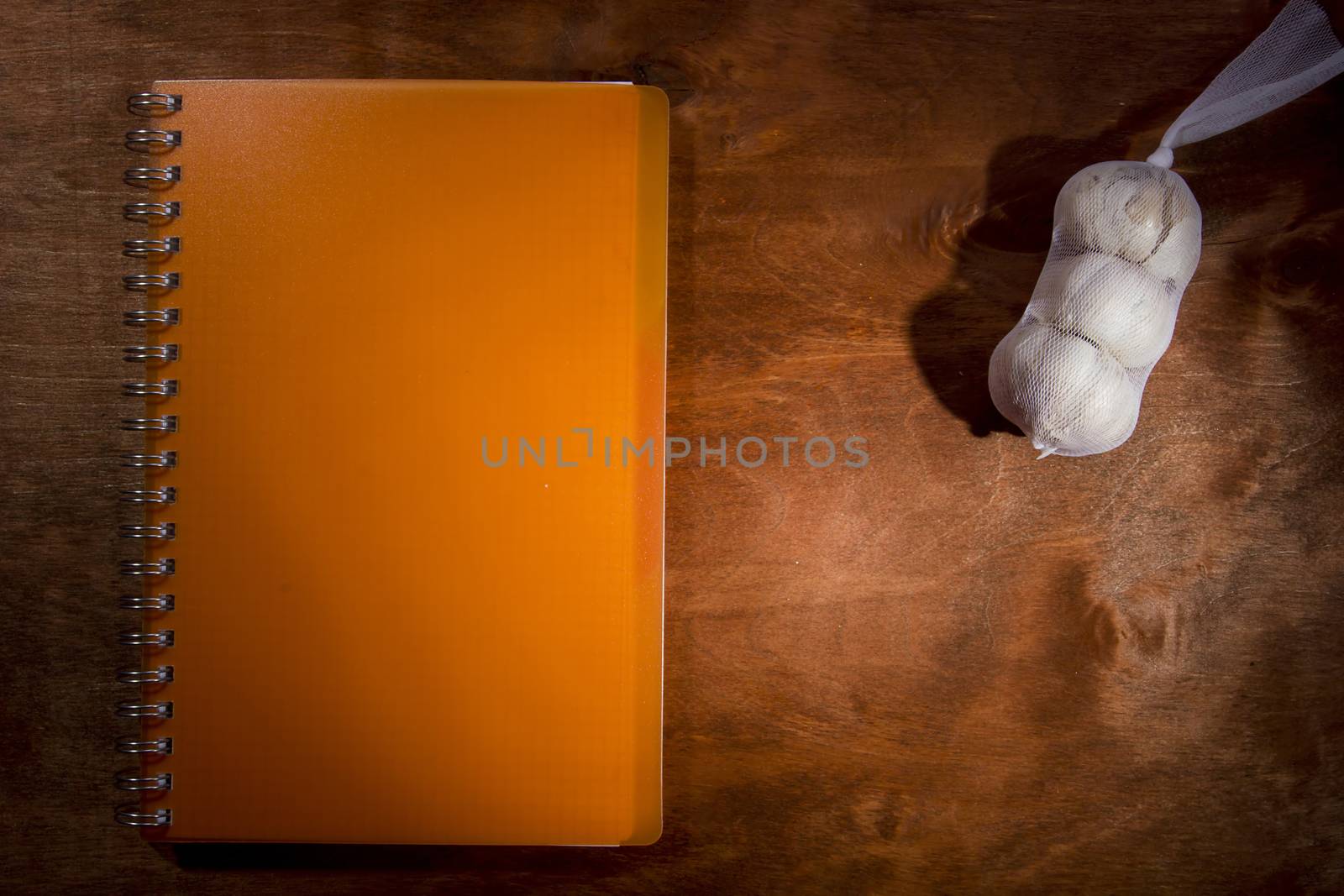 Garlic heads and orange notebook on a wooden table