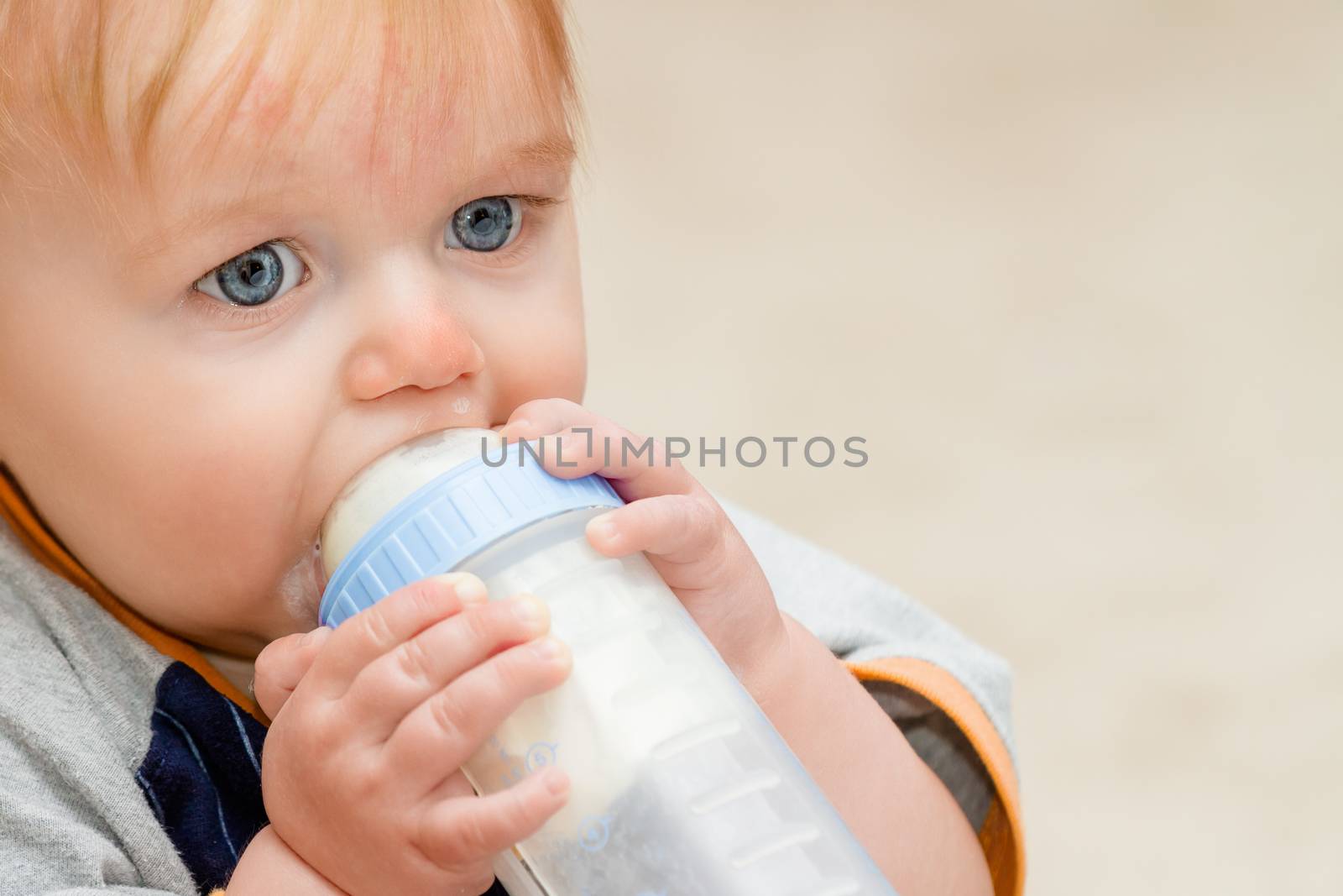 Boy with a milk bottle up to his mount drinking away while seated. There is some milke leakage around the mount and upper lip