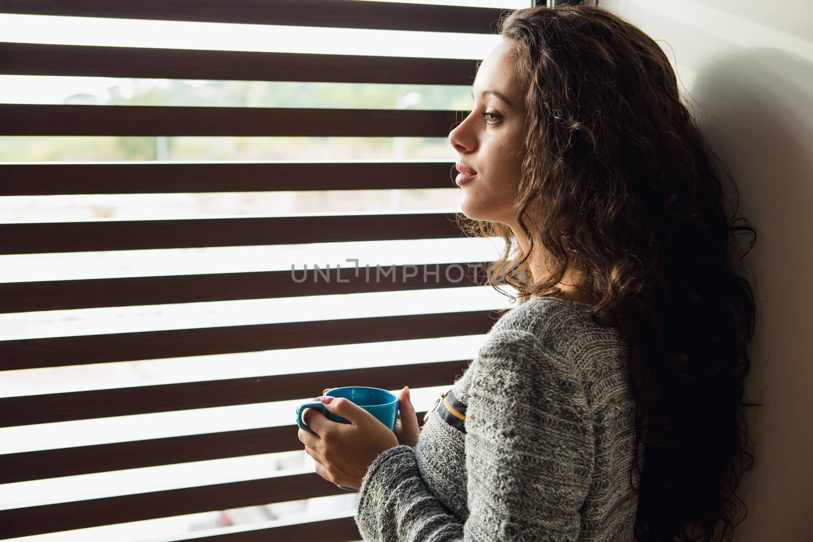 Beautiful woman looking through a window and drinking coffee
