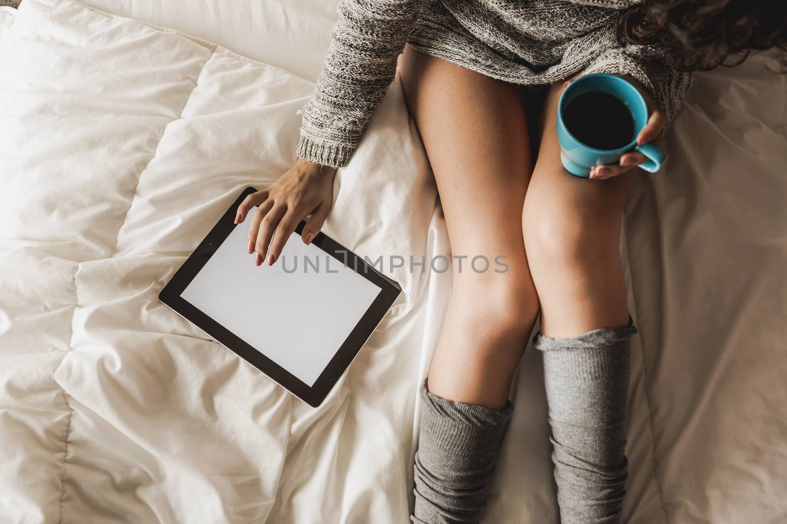 Woman on bed drinking and using a tablet