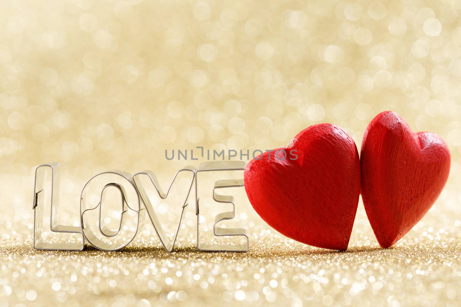 Two red handmade wooden hearts and word love on golden bright glitter lights bokeh background