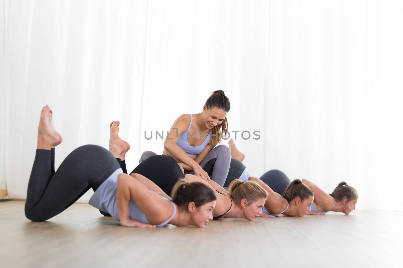 Group of young sporty sexy women in yoga studio, practicing yoga lesson with instructor, forming a line in front bent puppy dog asana pose. Healthy active lifestyle, working out indoors in gym.