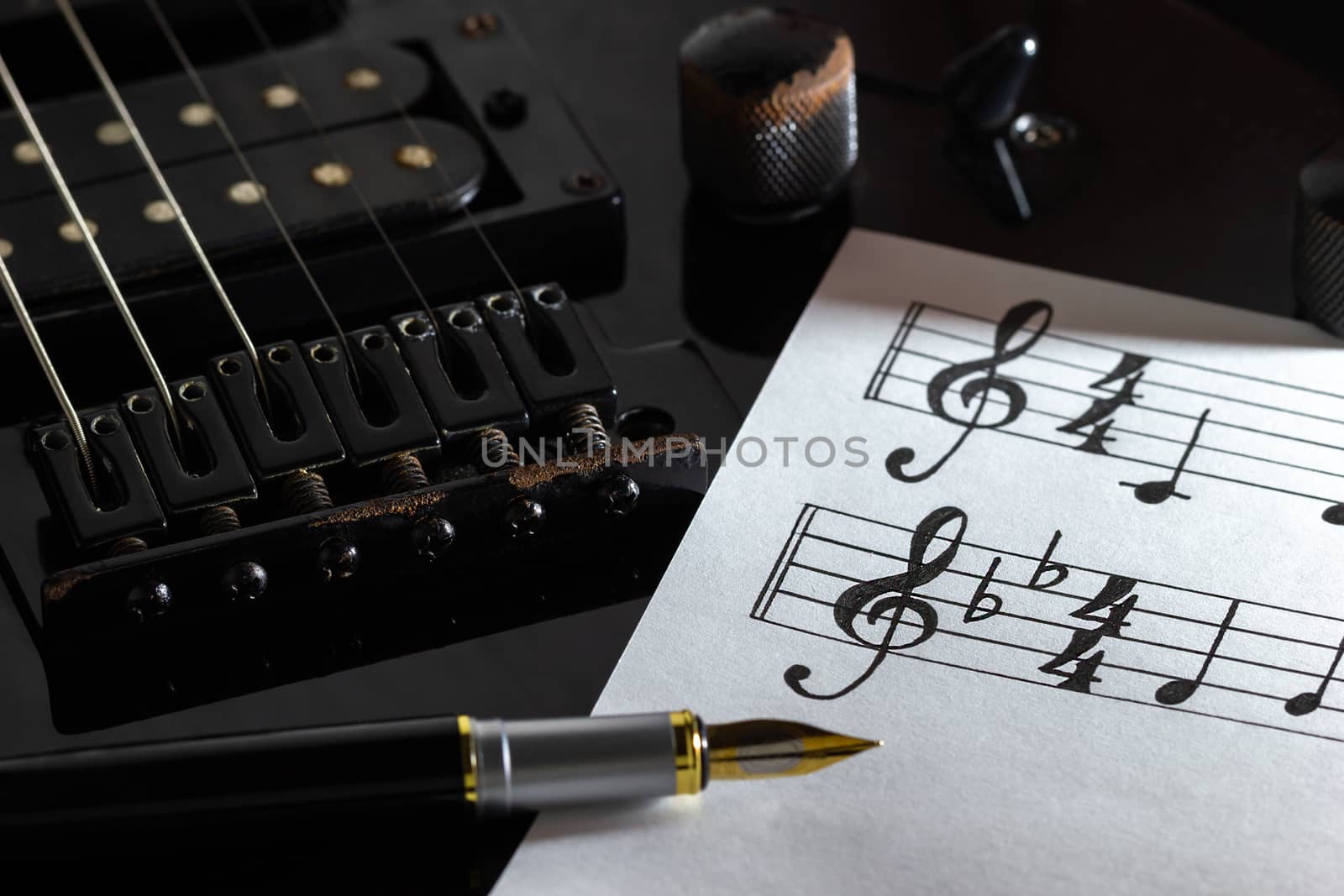 Music note and vintage pen on black electric guitar in darkness. by SaitanSainam