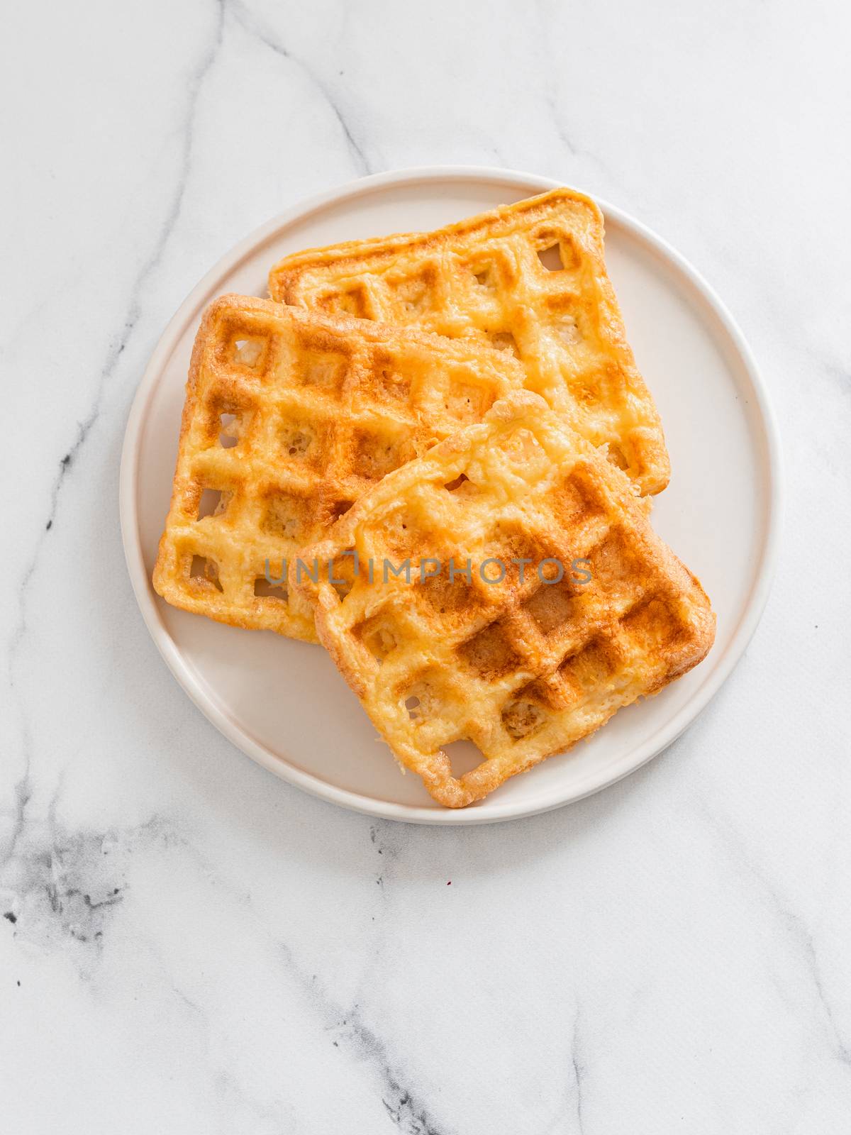 Perfect savory keto waffles. Two ingredients chaffles on plate over white marble background. Eggs and parmesan cheese low carb waffles. Top view or flat lay. Copy space for text or design. Vertical.