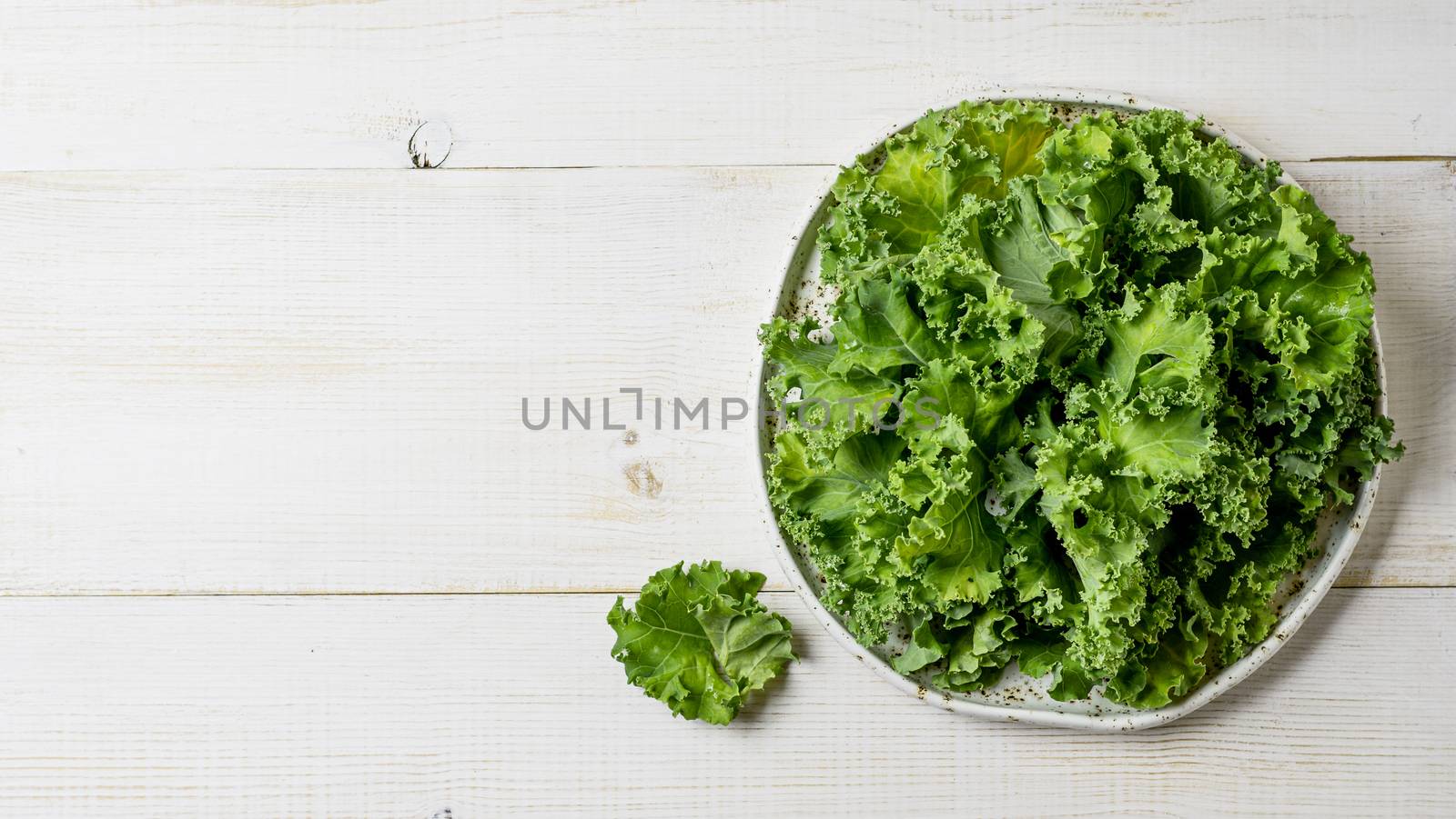 Kale close up. Green vegetable leaves, top view on white craft plate over white wooden tabletop. Healthy eating, vegetarian food,dieting concept. Top view or flat lay. Copy space. Health kale benefits