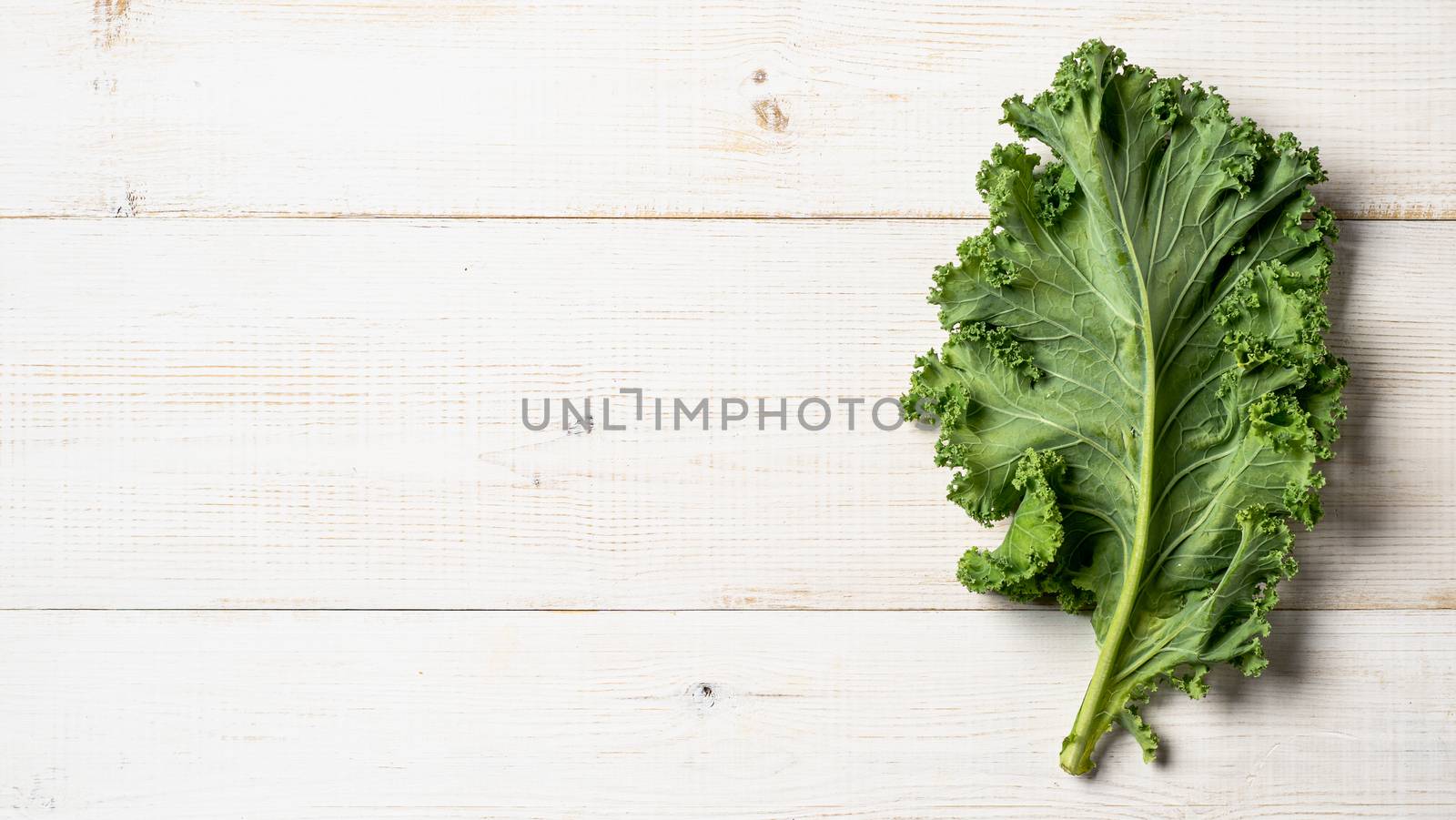 Fresh green kale leaf on white wooden tabletop. Healthy detox vegetables. Vegetarian food, healthy eating, dieting concept. Top view or flat lay. Copy space. Health kale benefits. Banner