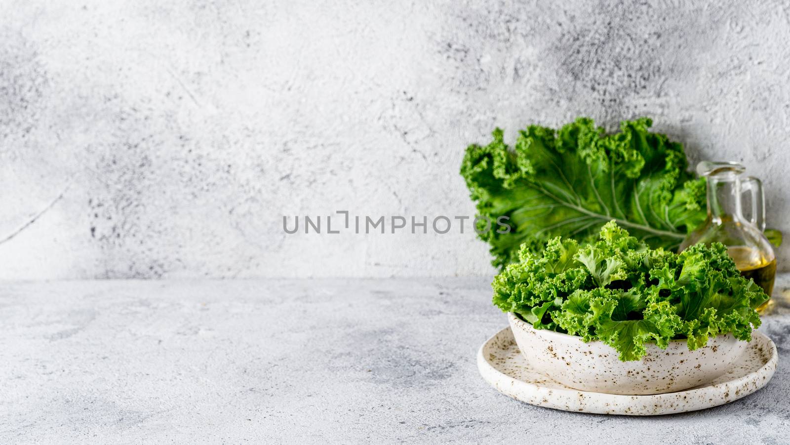 Green kale leaves in white craft bowl on gray cement background. Healthy eating, vegetarian food, dieting concept. Copy space left. Health kale benefits. Banner