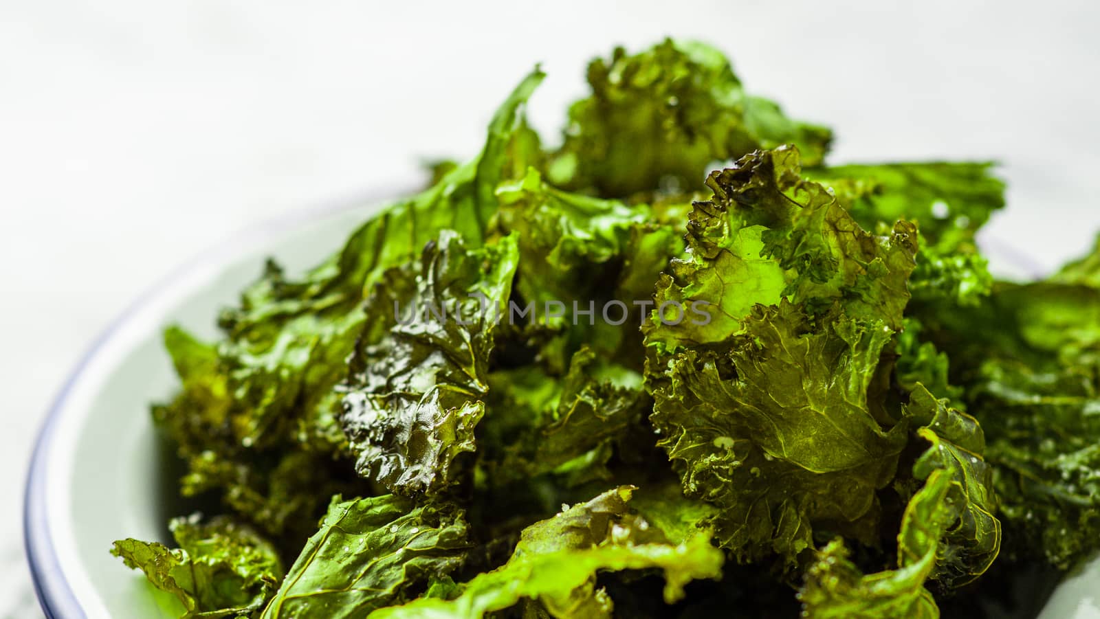 Green Kale Chips with salt close up. Homemade healthy snack for low carb, keto, low calorie diet. Ready-to-eat kale chips, copy space left. Banner