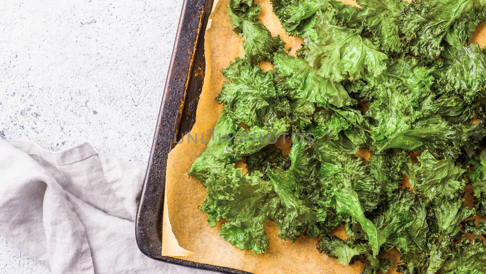 Green Kale Chips with salt on oven-tray. Homemade healthy snack for low carb, keto, low calorie diet. Gray cement background. Ready-to-eat kale chips, copy space for text. Banner