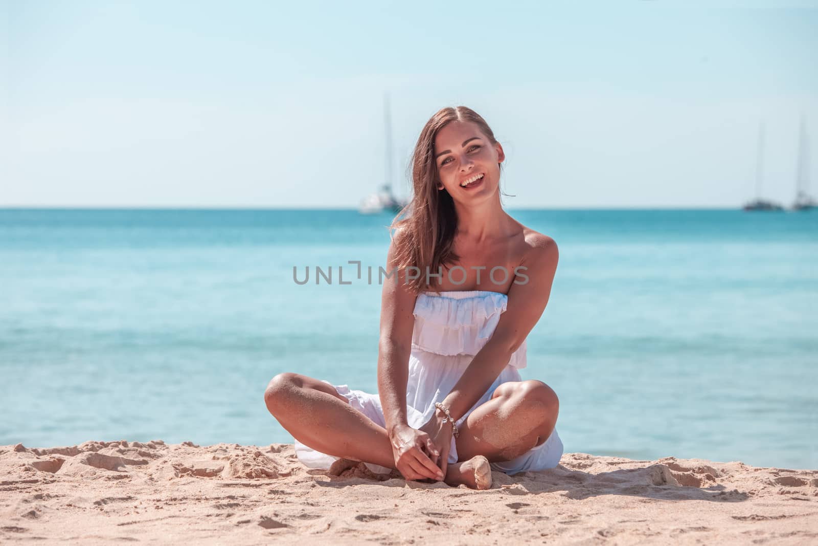 Happy woman enjoying vacation. Beautiful woman in white dress Sitting on the beach