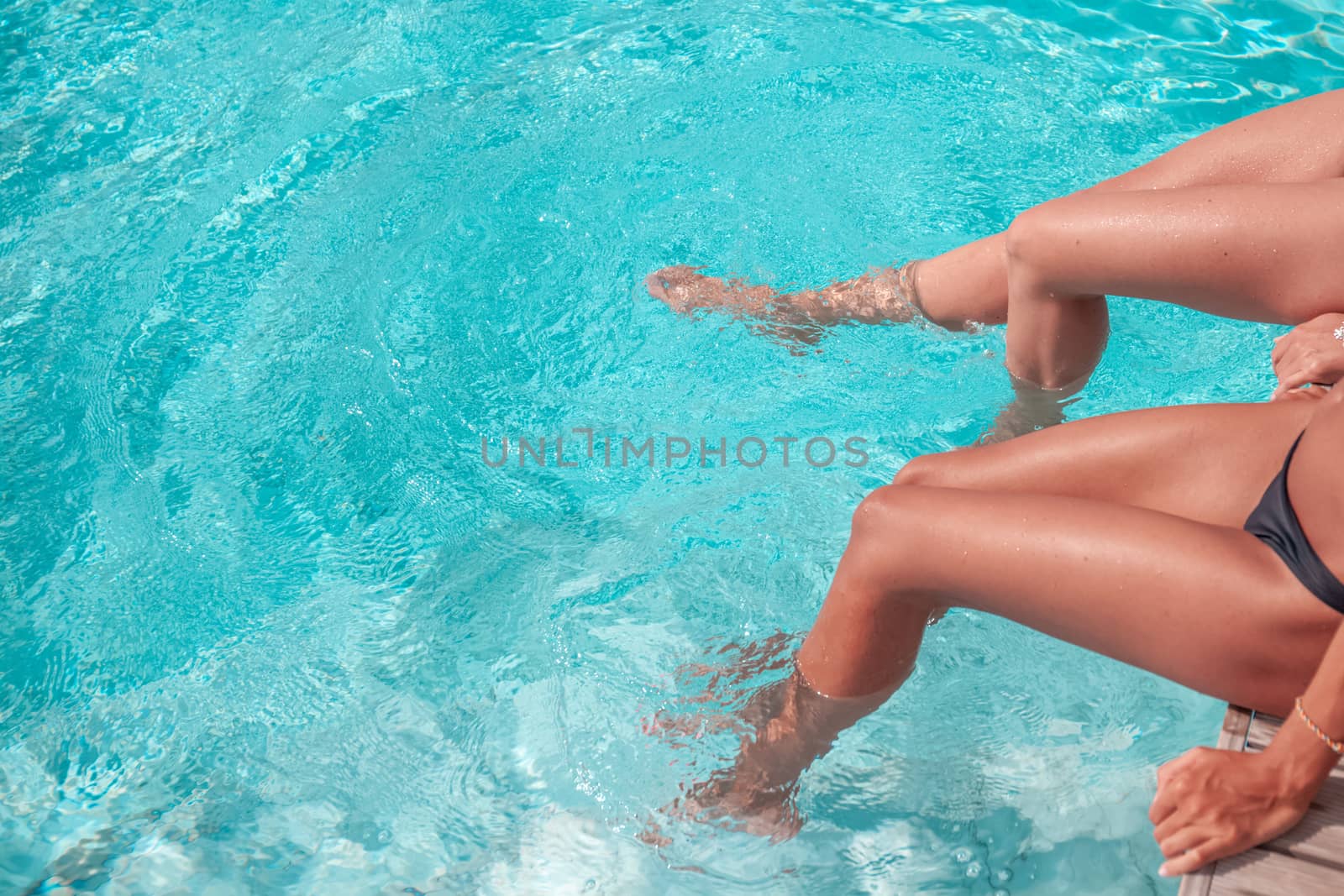 Female friends legs in the swimming pool copy space for text