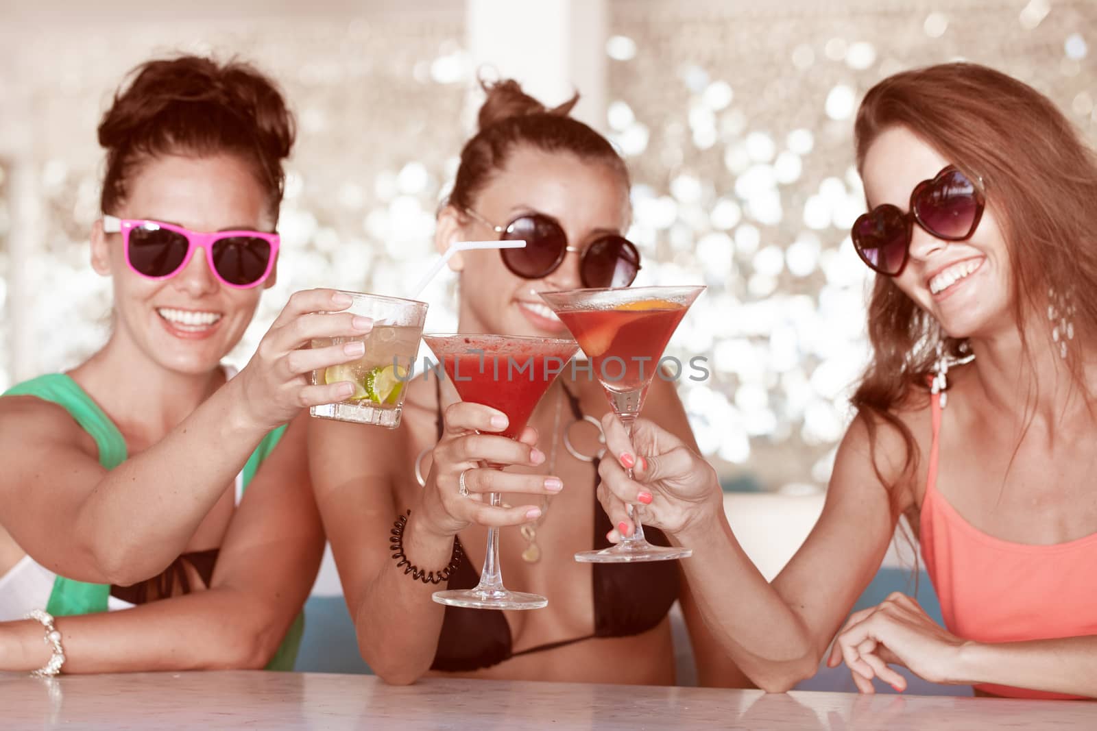 Three female friends sitting in summer cafe drinking cocktails