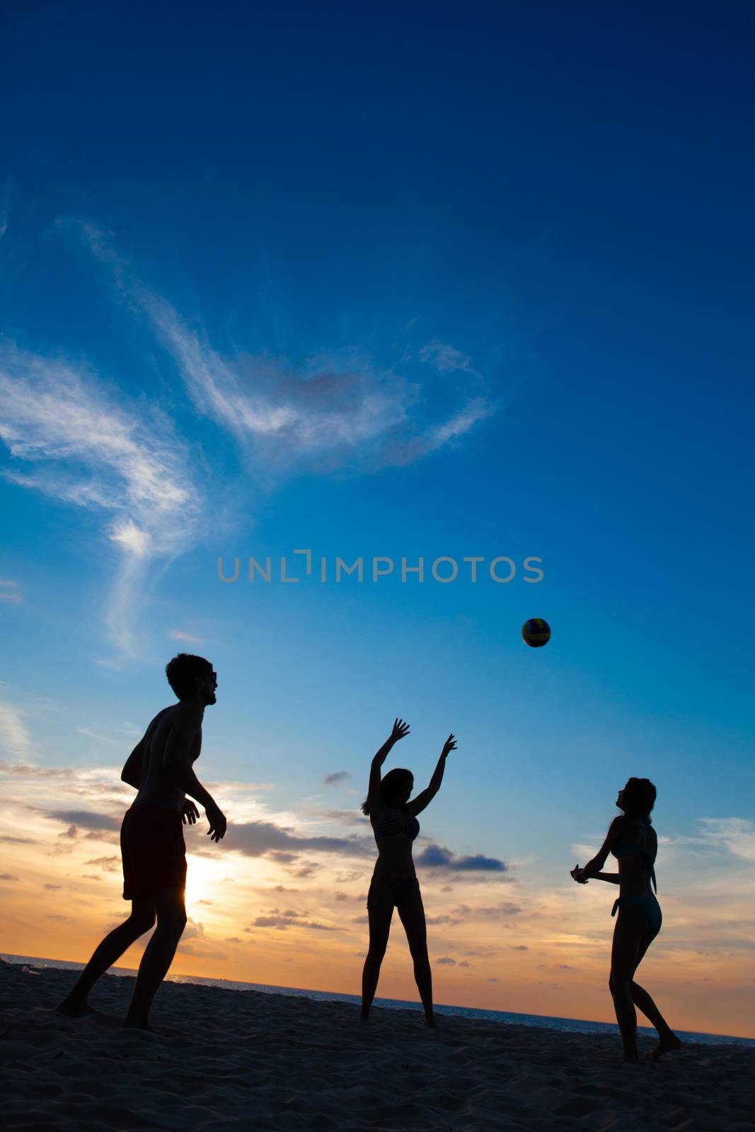 Group of young people playing volleyball on beach at sunset