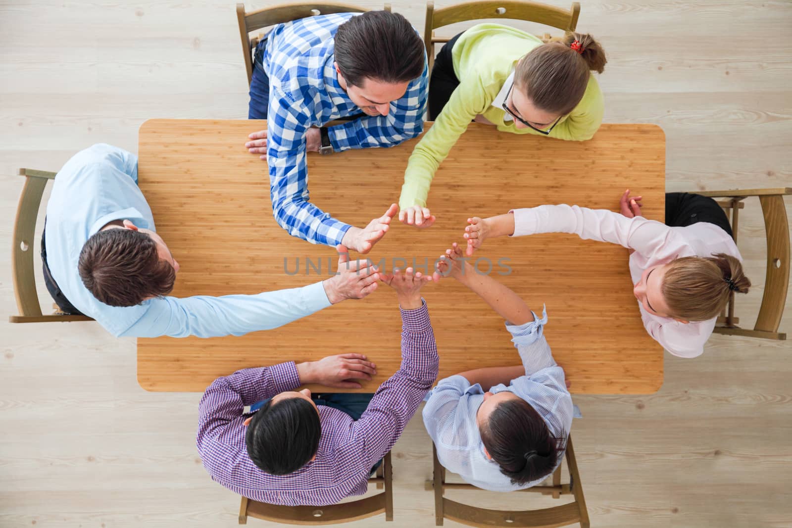 Coworkers doing high five sitting at the office table, top view