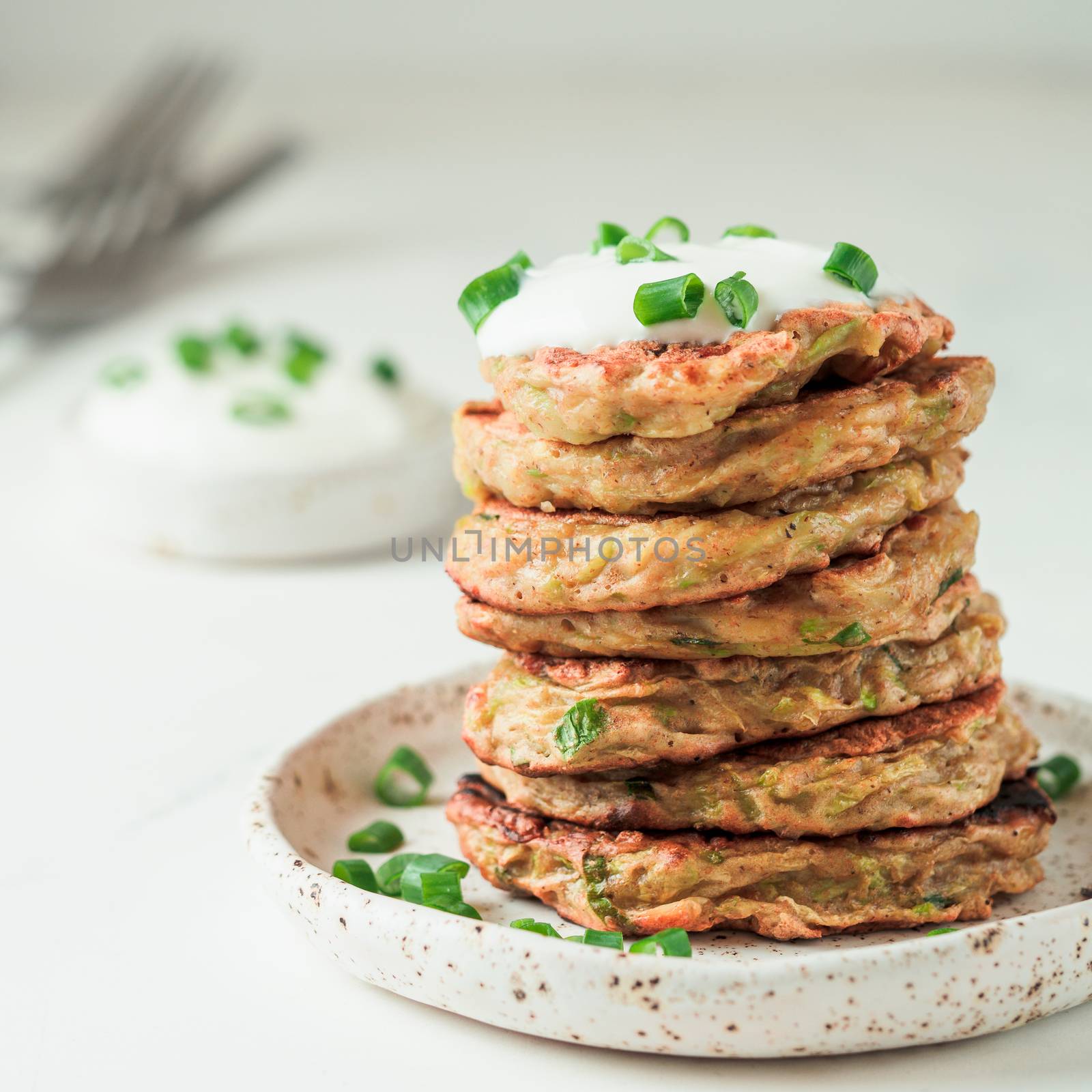 Zucchini fritters. Traditional zucchini fritters in stack on white background. Zucchini pancakes or fritters with green onion and parmesan cheese,served sour cream or greek yogurt. Copy space for text