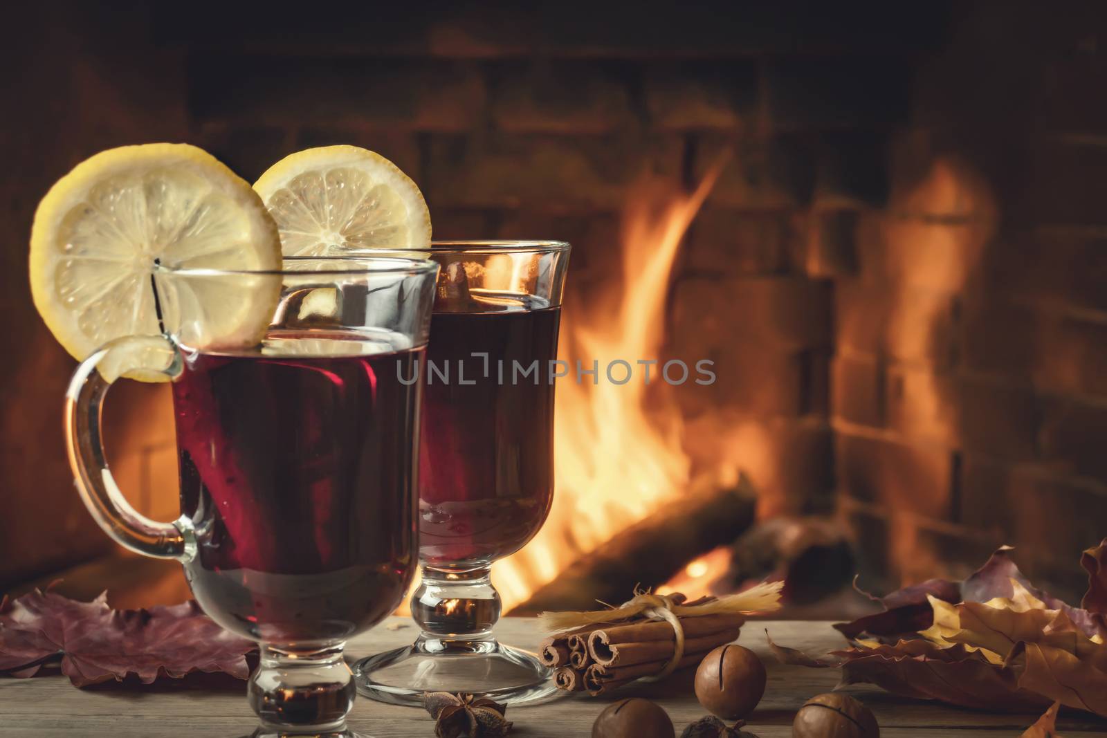 Two glasses of mulled wine on a wooden table in front of a burning fireplace by galsand