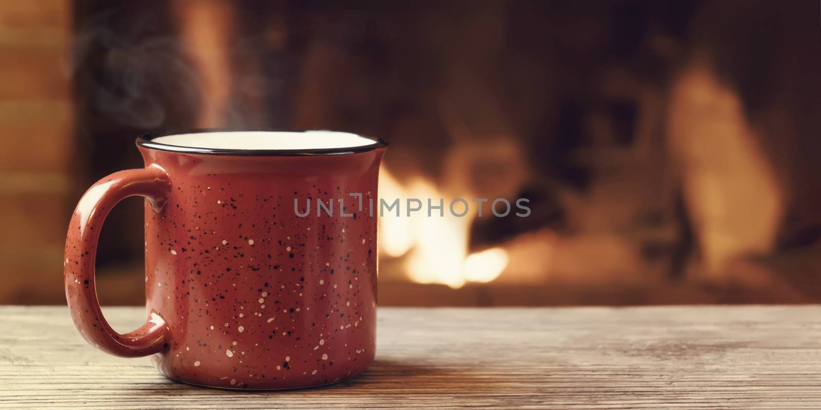 Red mug with hot tea in front of a burning fireplace, comfort, winter holidays and warmth of the hearth concept by galsand